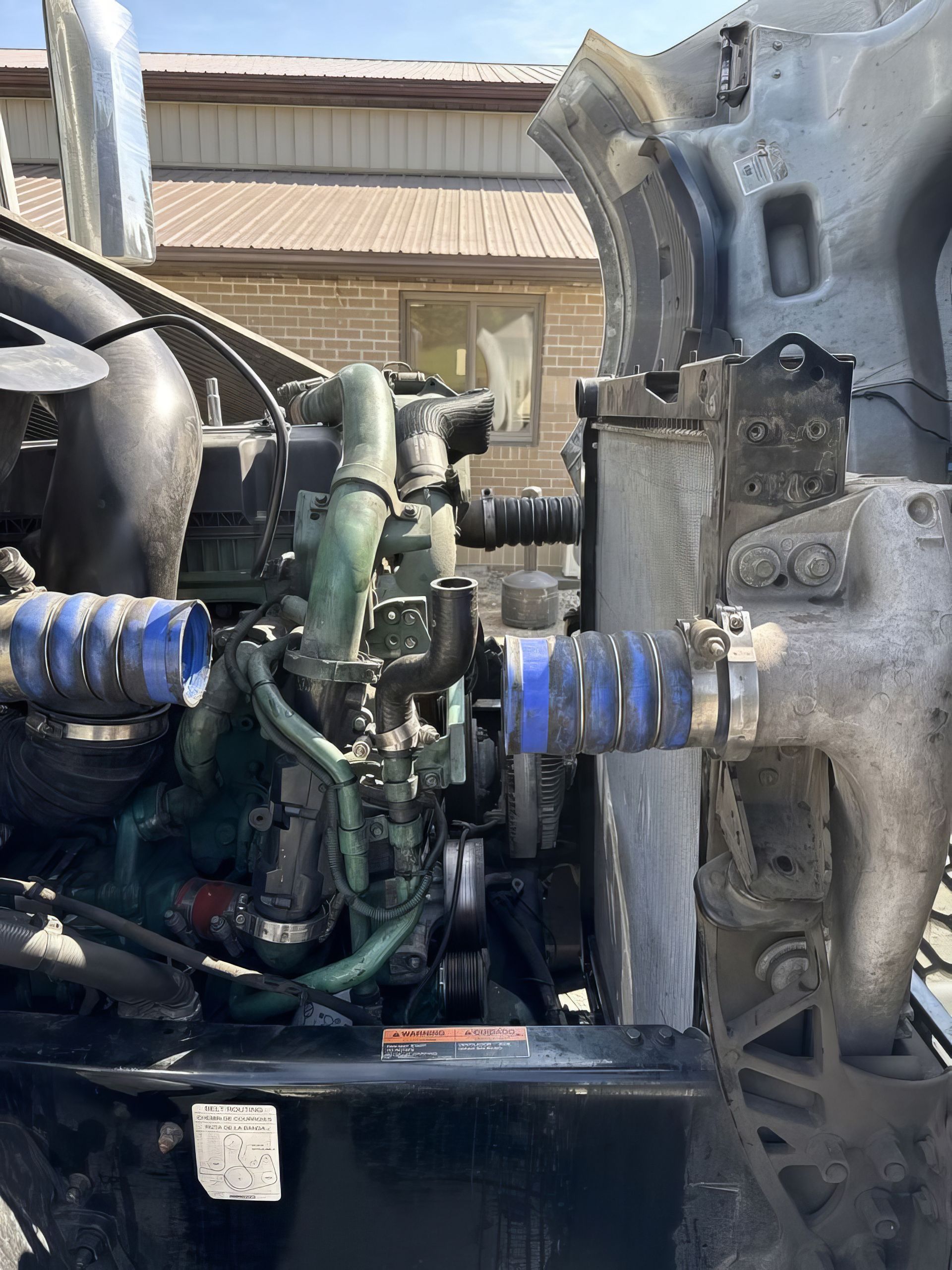 Close-up of a truck engine compartment with hoses, metal parts, and a blue spring suspension visible