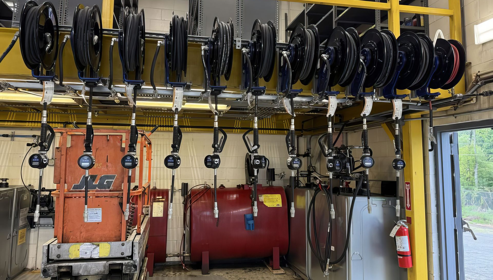 Industrial hose and cable reels mounted on a wall in a utility room with red tanks and valves.