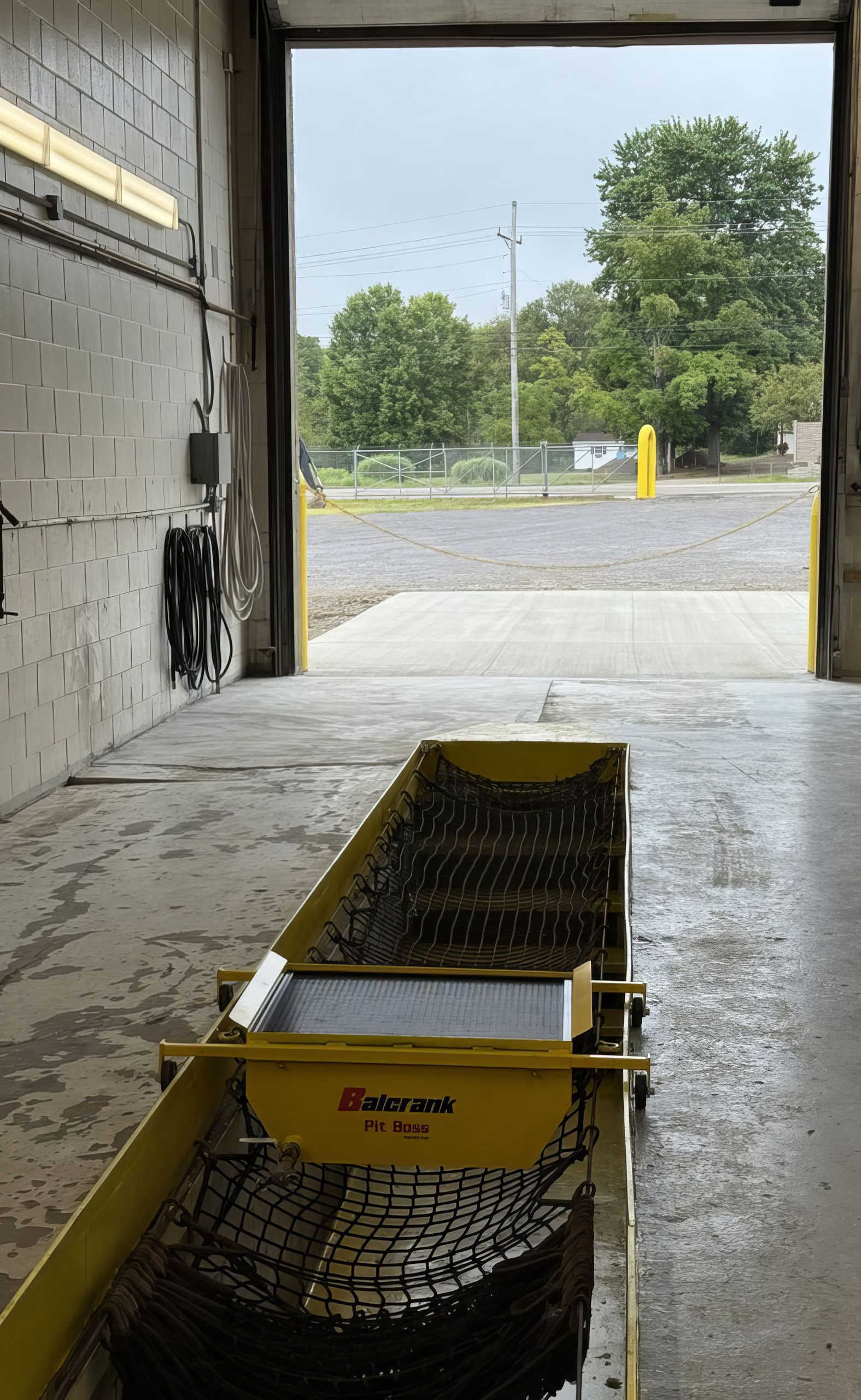 Yellow industrial cart in a garage opening onto a gravel lot and trees