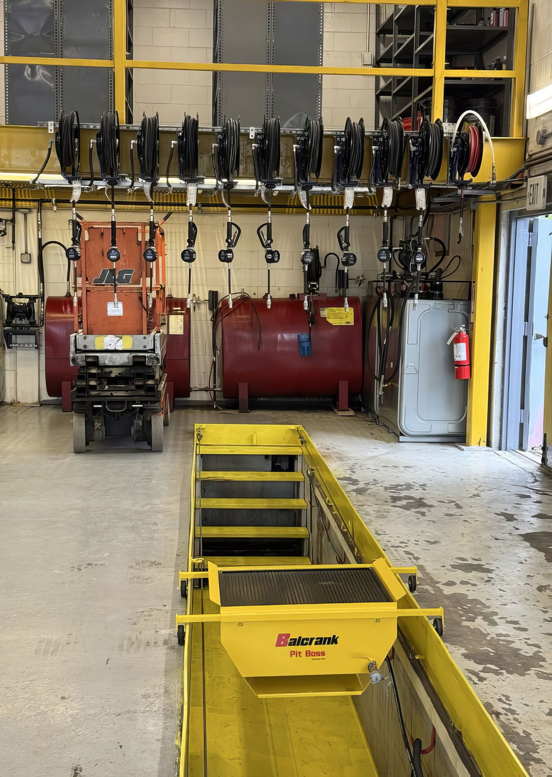 Industrial maintenance bay with a yellow lift platform, overhead equipment, and large tanks in the background