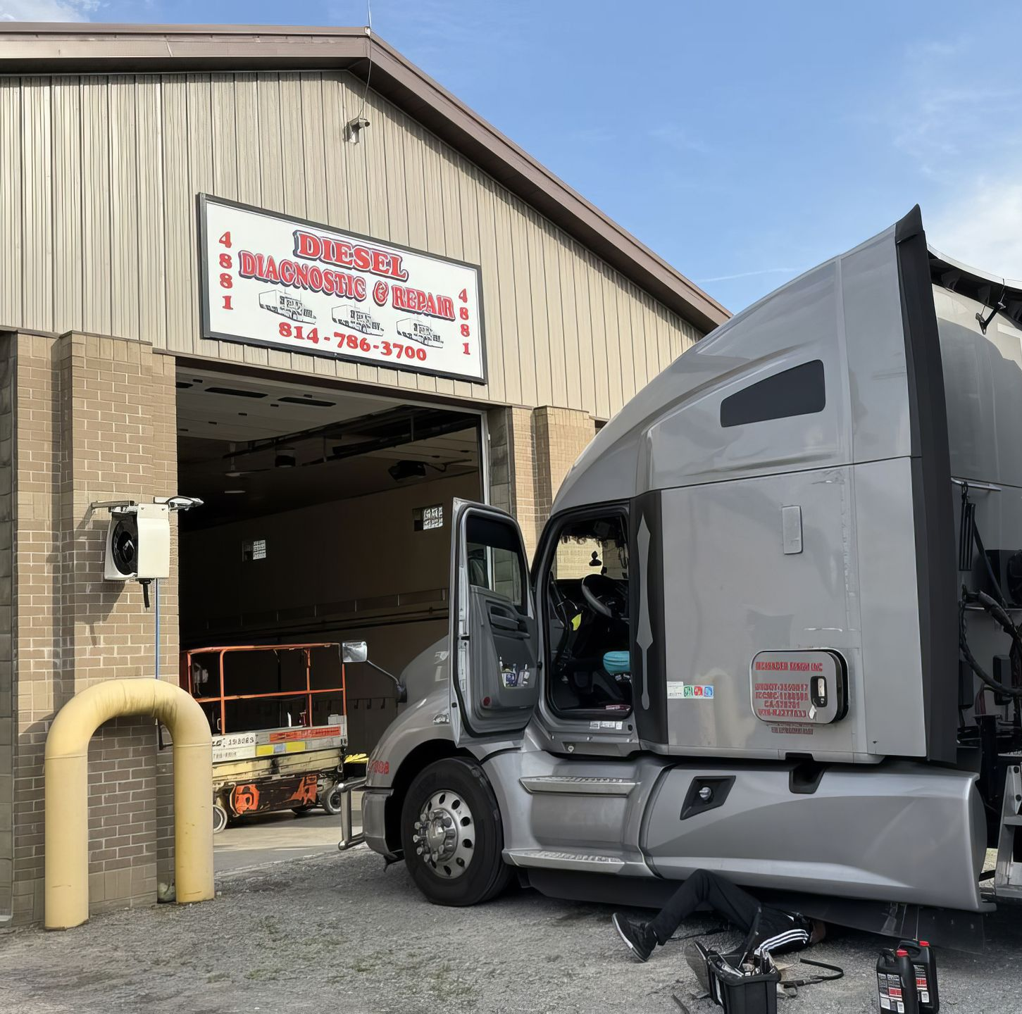 Gray semi-truck parked at warehouse loading dock with open cab door and forklift inside bay
