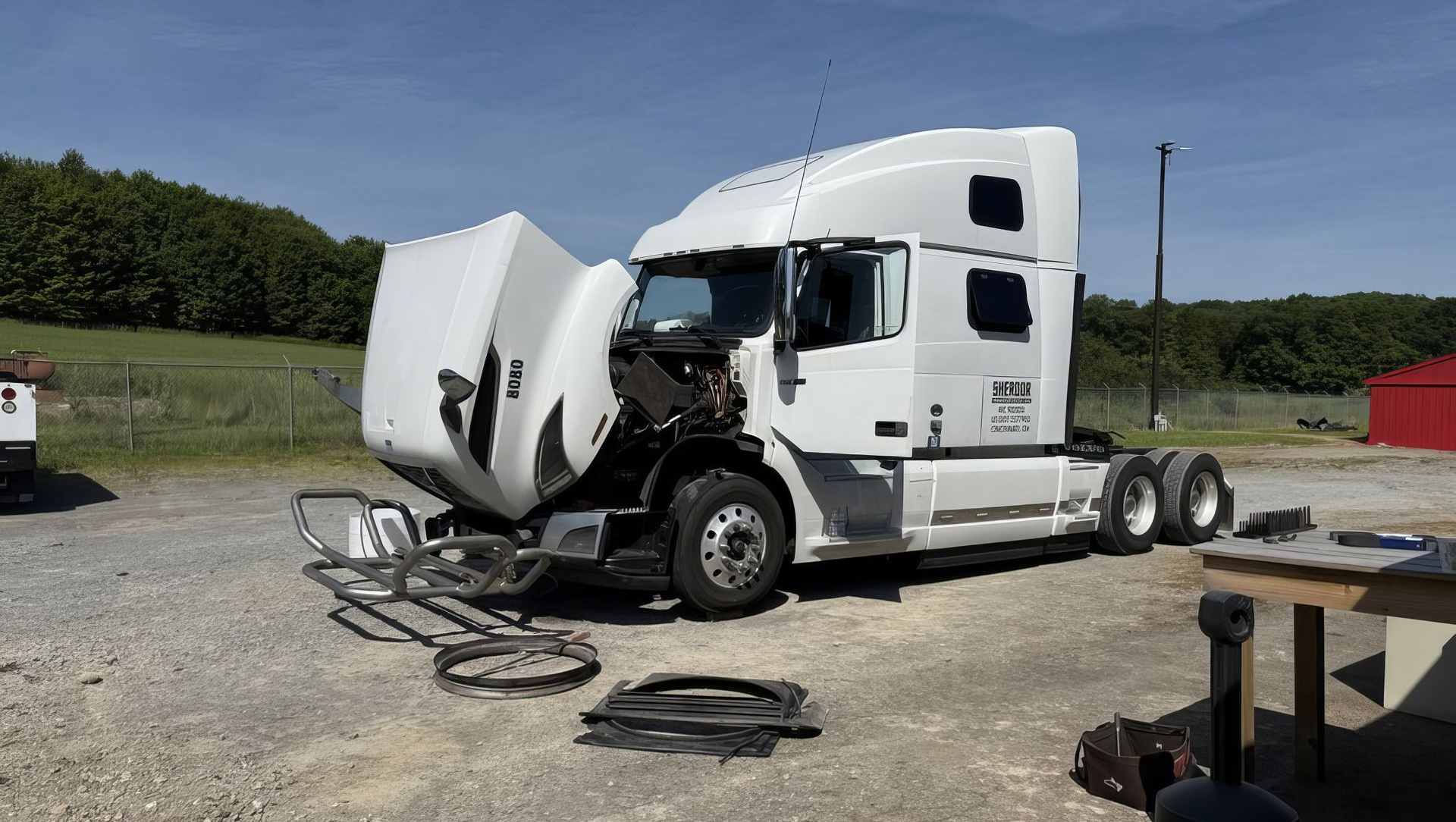 White semi-truck with front-end damage parked in a gravel lot under clear sky.