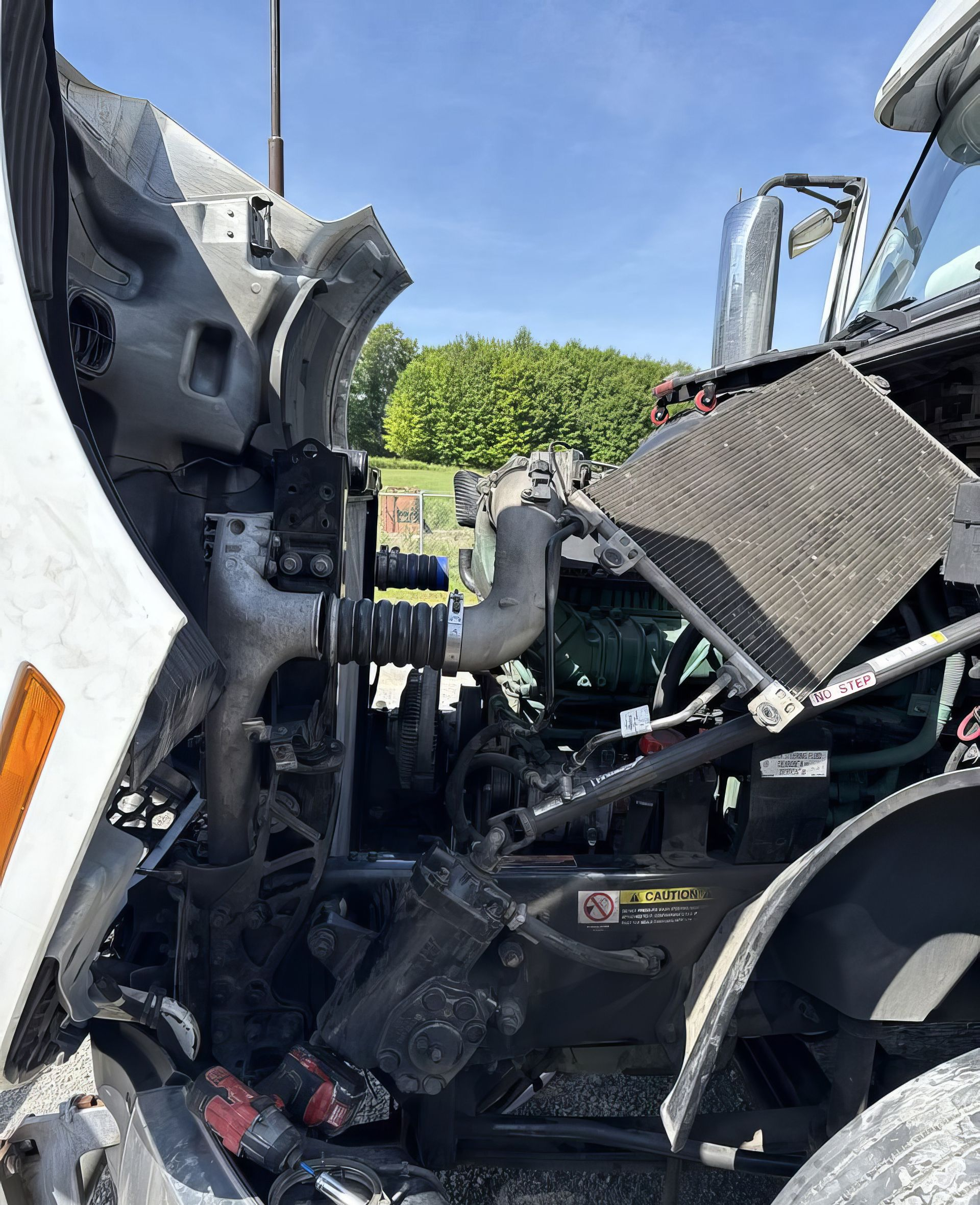 Severe truck cab collision damage with crushed metal and exposed engine parts under a blue sky