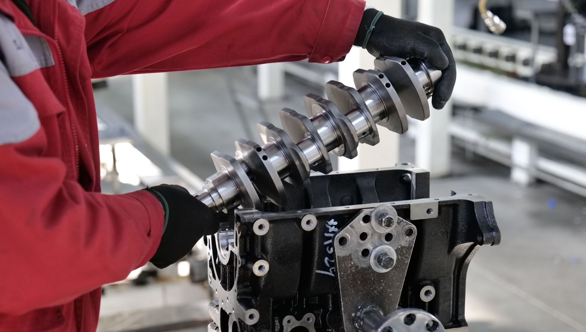 Mechanic in red jacket assembling a car engine with a metal crankshaft in a workshop