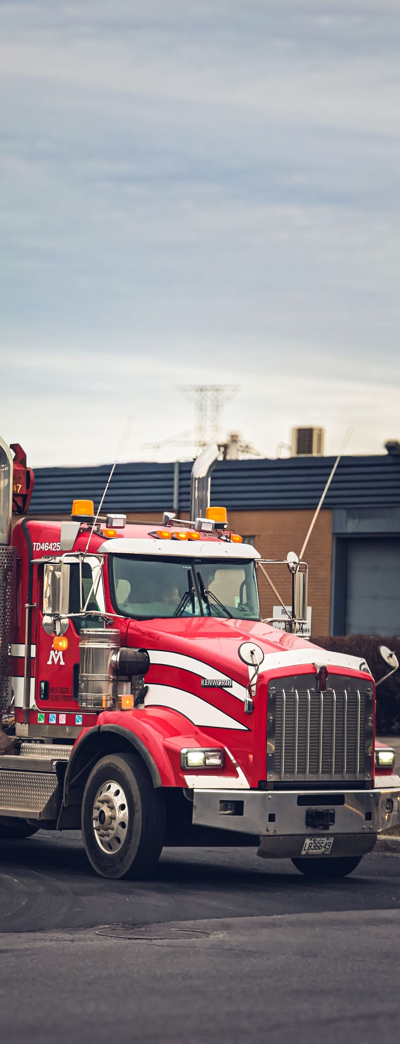 Red semi-truck parked outdoors in front of a low building under a cloudy sky