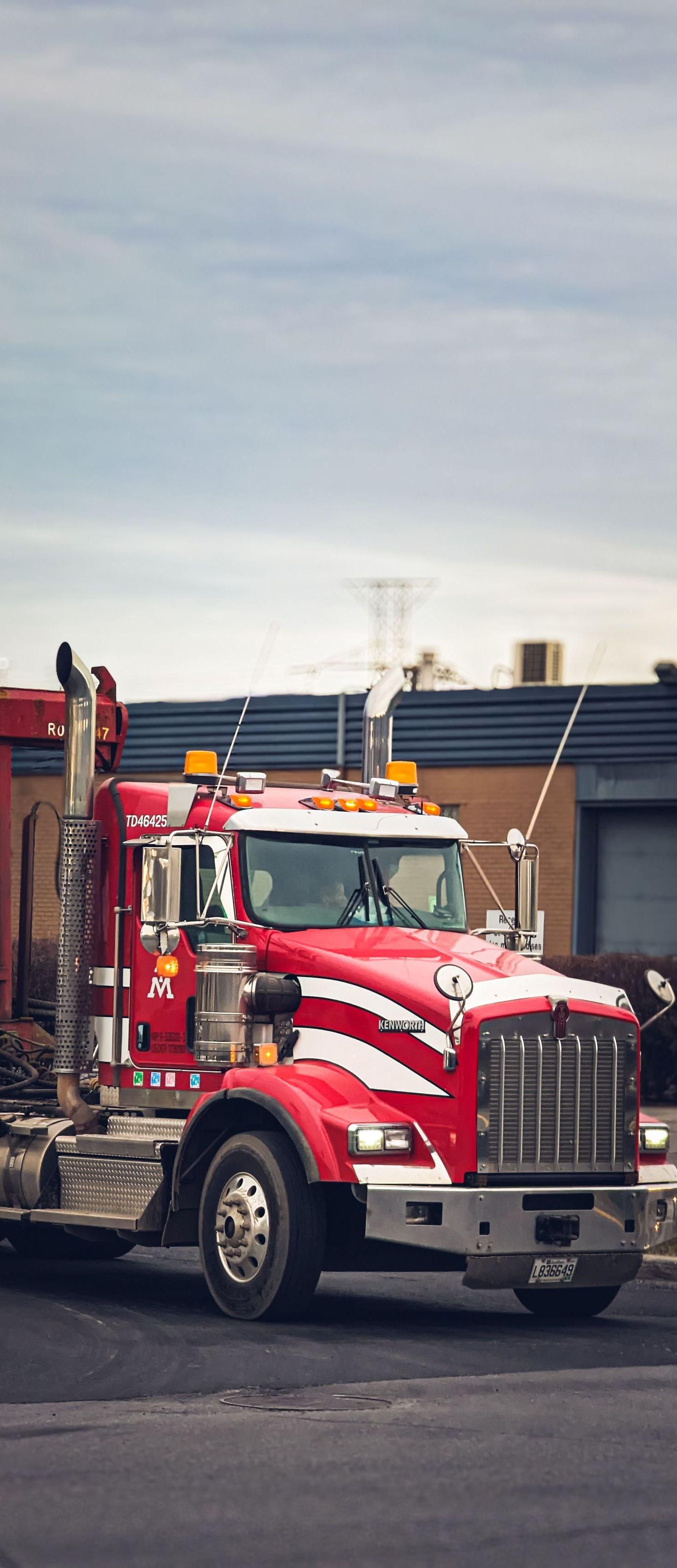 Red and white tow truck parked in a lot beside a building, with a cloudy sky overhead.