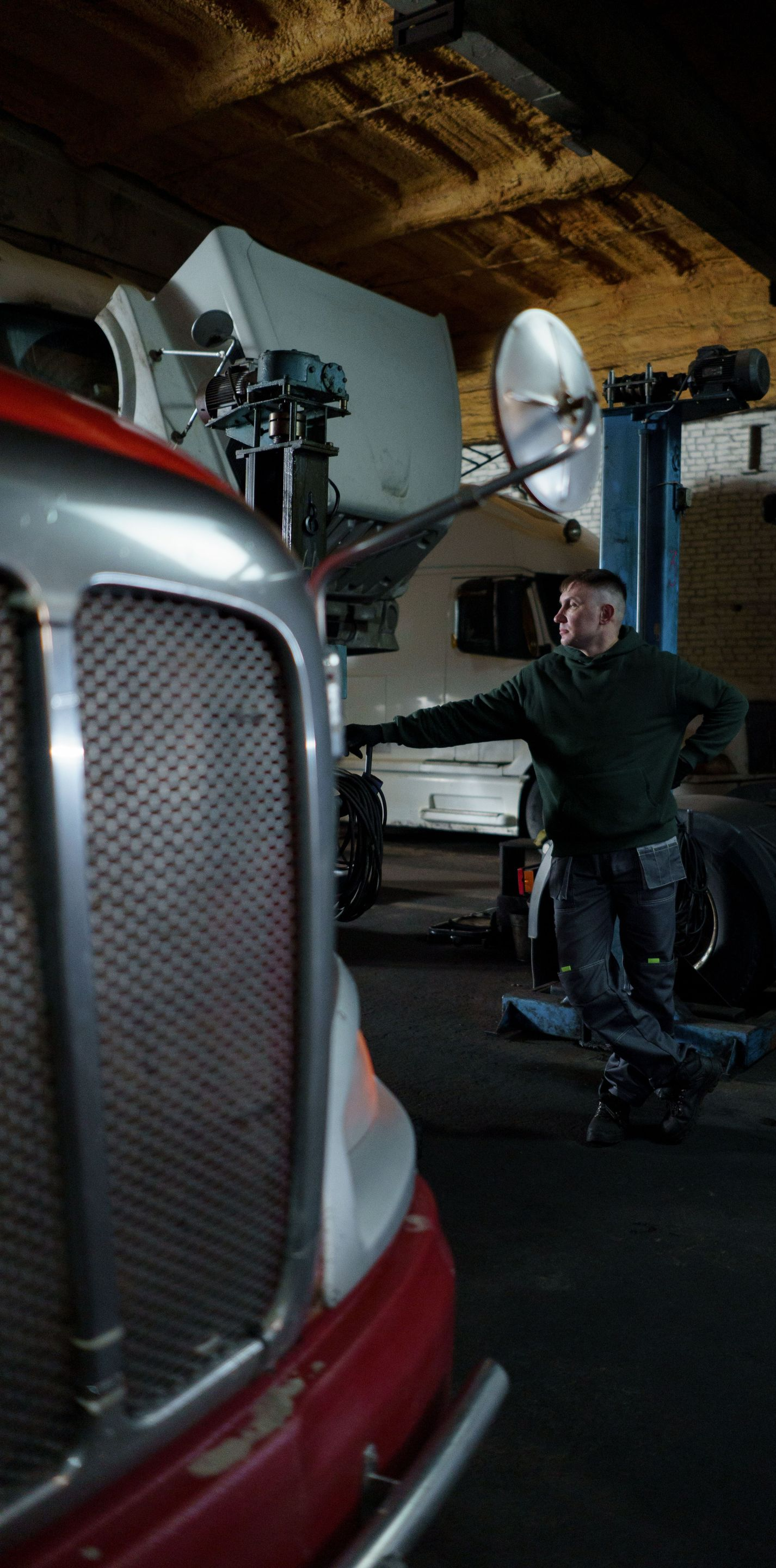 Man standing beside a red truck and white RV inside a garage, with a large satellite dish in the background