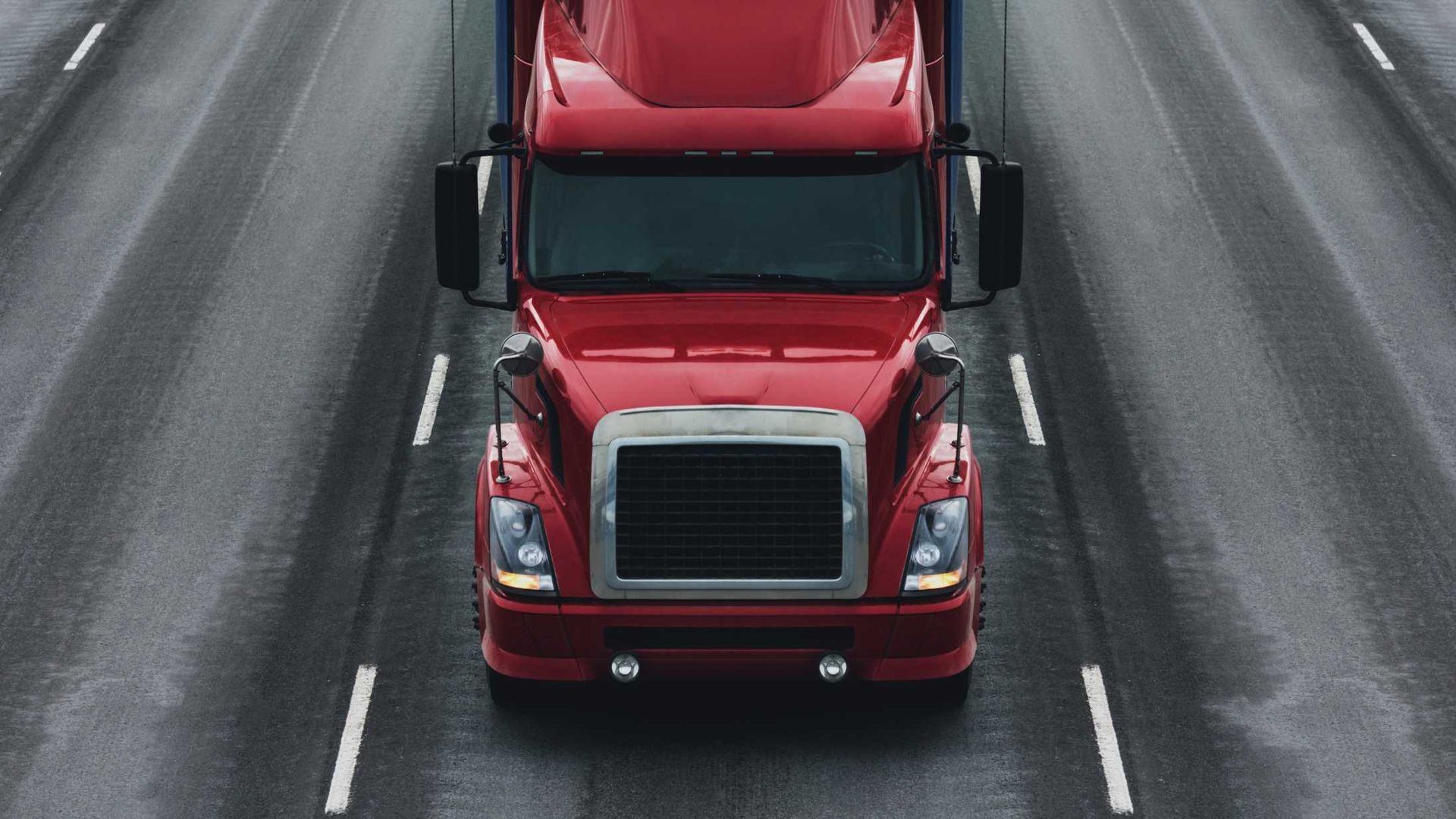 Red semi-truck driving on a wet highway, centered in its lane