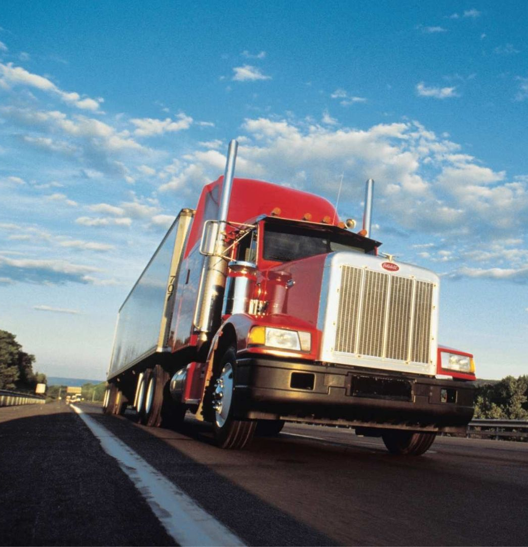 Red semi-truck driving on a highway under a blue sky with clouds