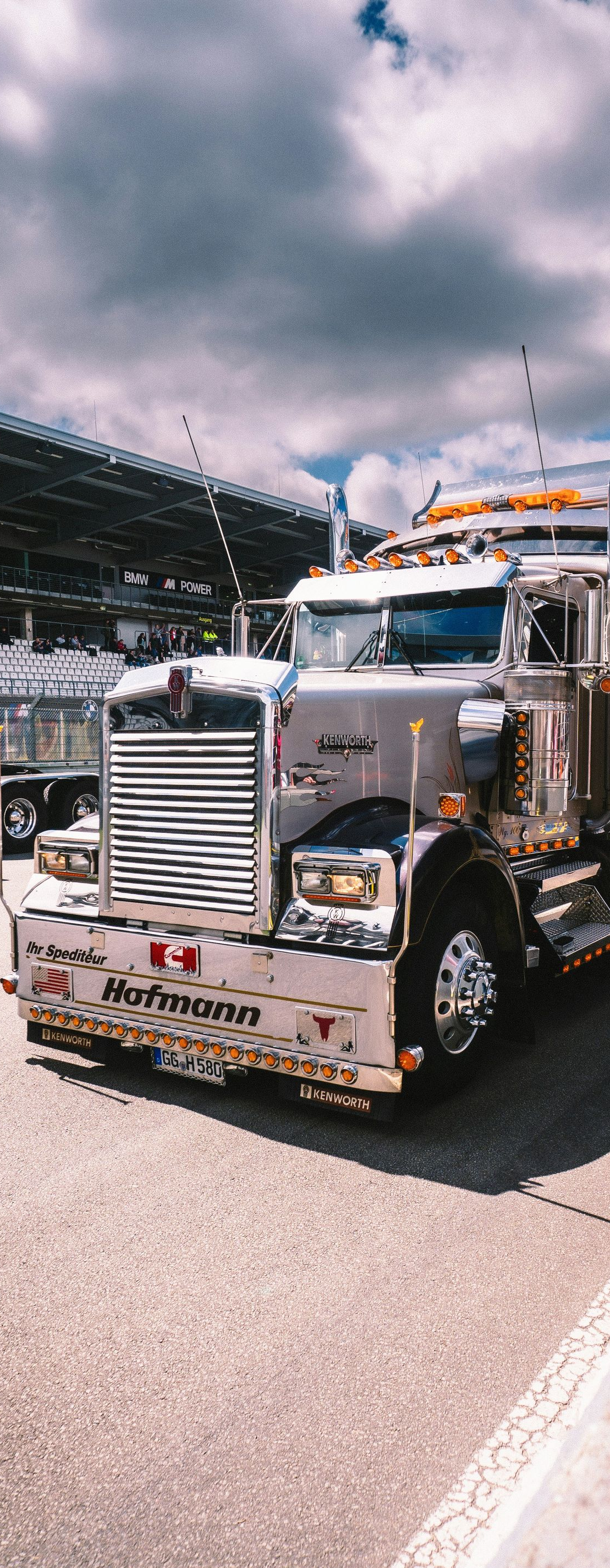 Chrome semi truck parked under cloudy skies at an outdoor event, front view with orange roof lights