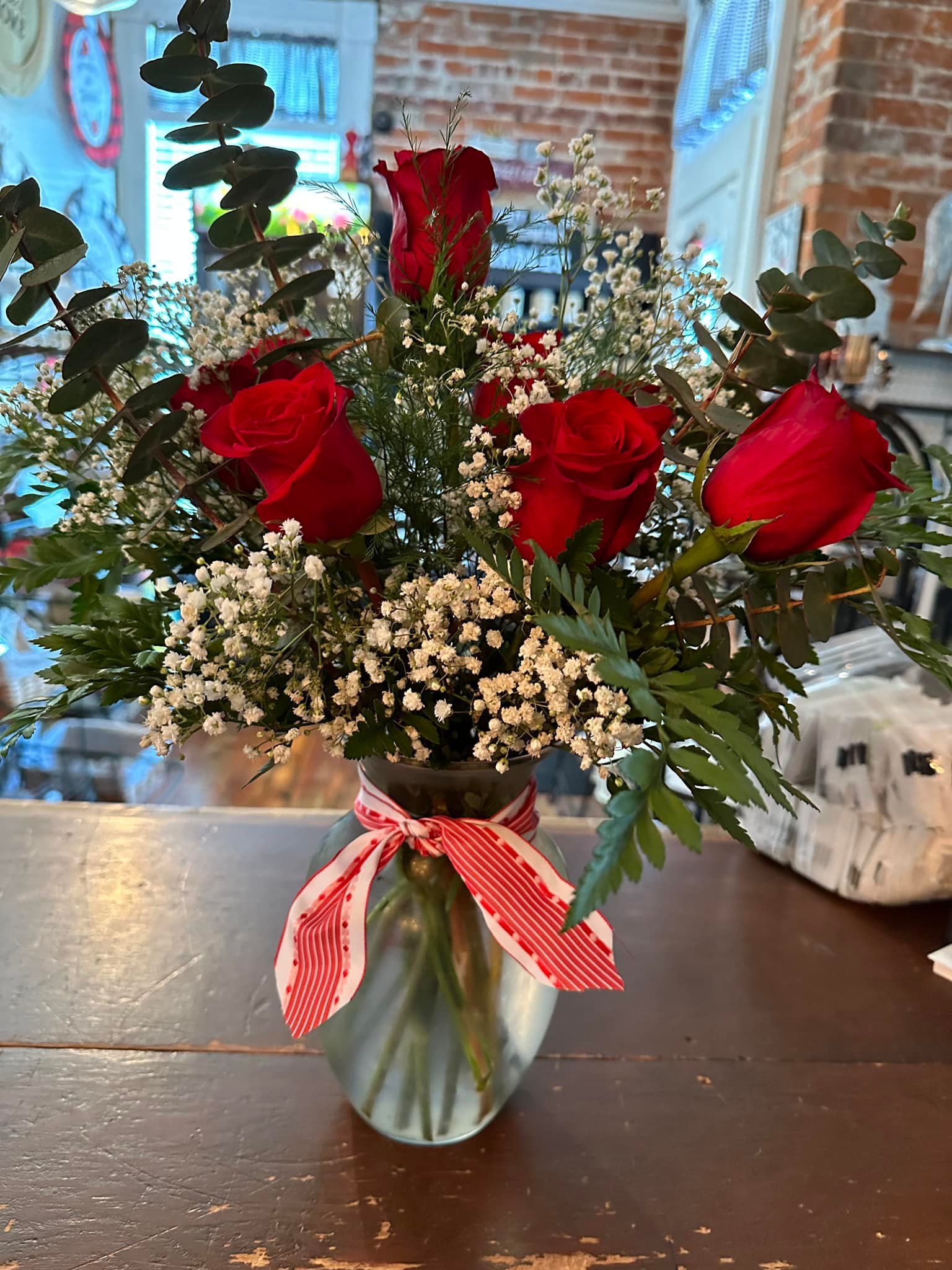 A vase filled with red roses and baby 's breath is sitting on a wooden table.
