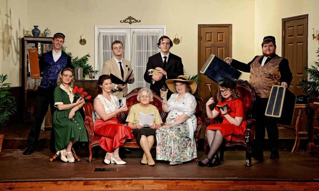 Group portrait of people in colorful period costumes posed in a living room with chairs and a piano