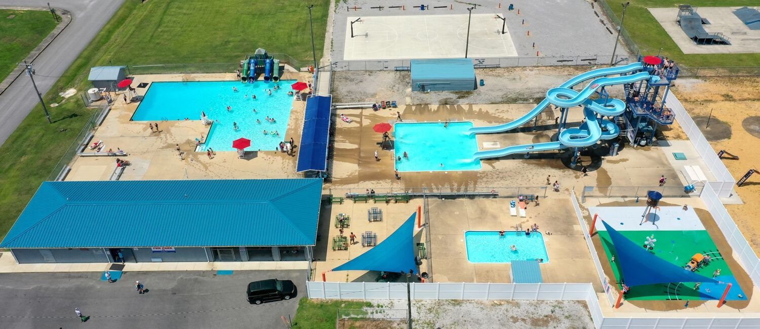 Aerial view of a water park with bright blue pools, slides, and play areas on a paved site.