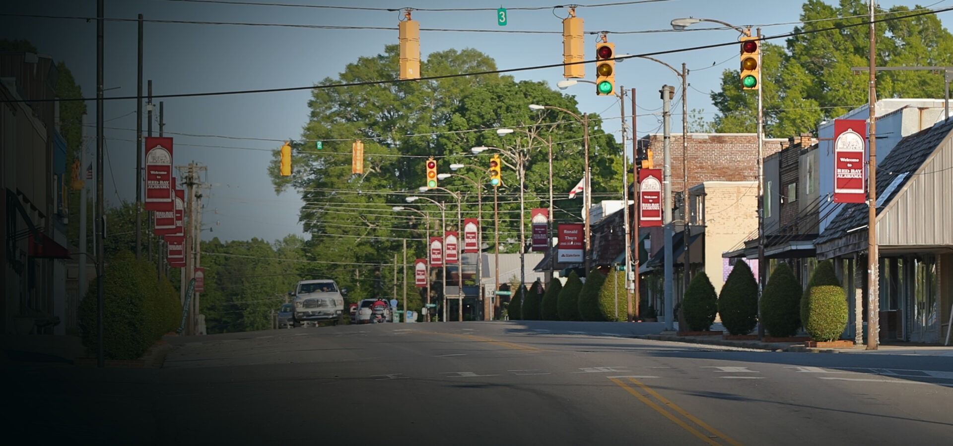 Quiet small-town street with storefronts, traffic lights, and trees on a sunny day