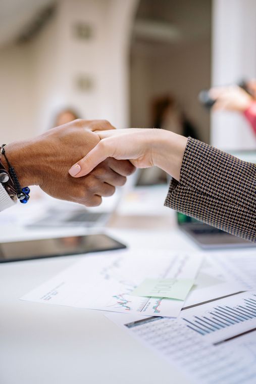 Two people shaking hands over documents on a desk in a bright office