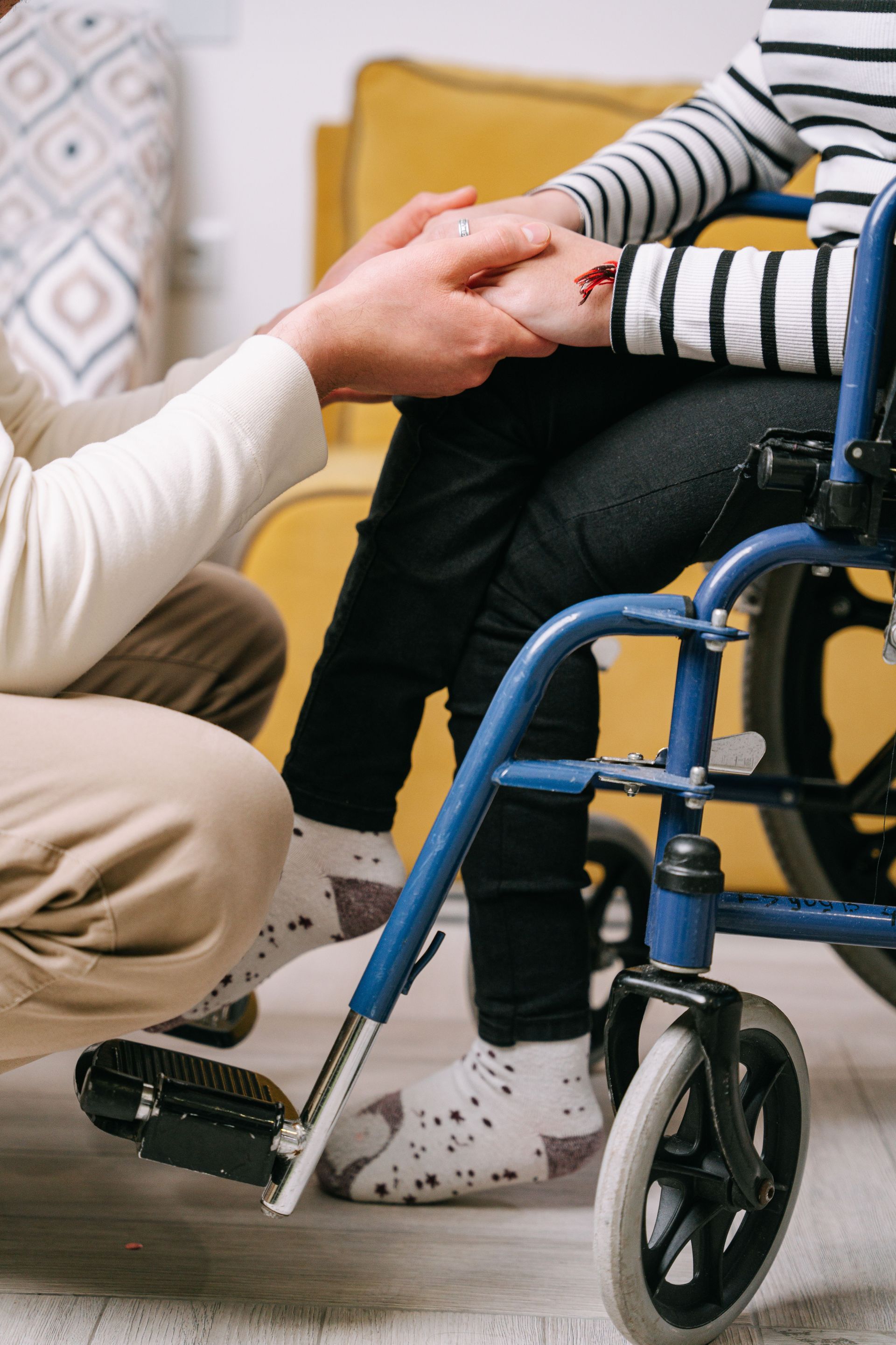 Person in wheelchair holding hands with another person indoors, showing support and connection.