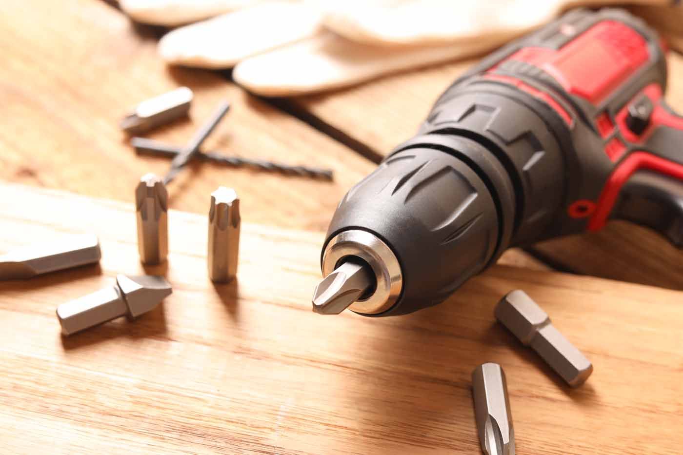 A close up of a drill and bits on a wooden table.