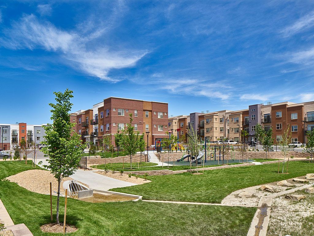 A playground with slides and a grassy lawn surrounded by modern apartment buildings under a blue sky.