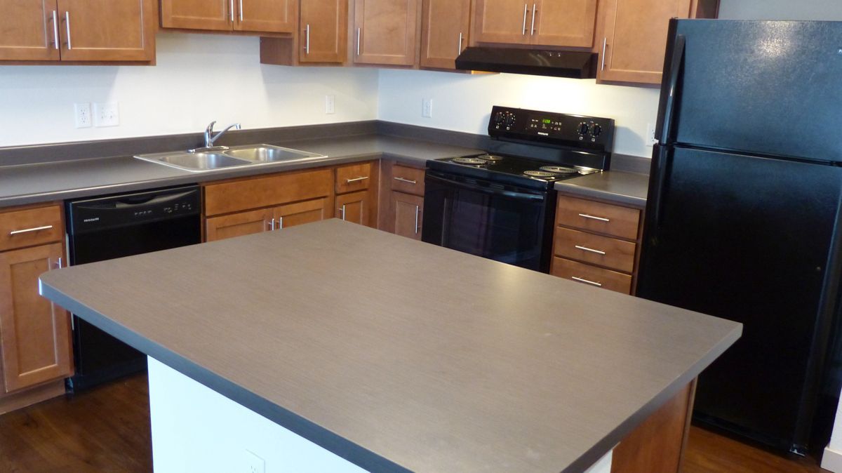 Kitchen with brown wooden cabinets, gray countertops, a kitchen island, and black appliances.