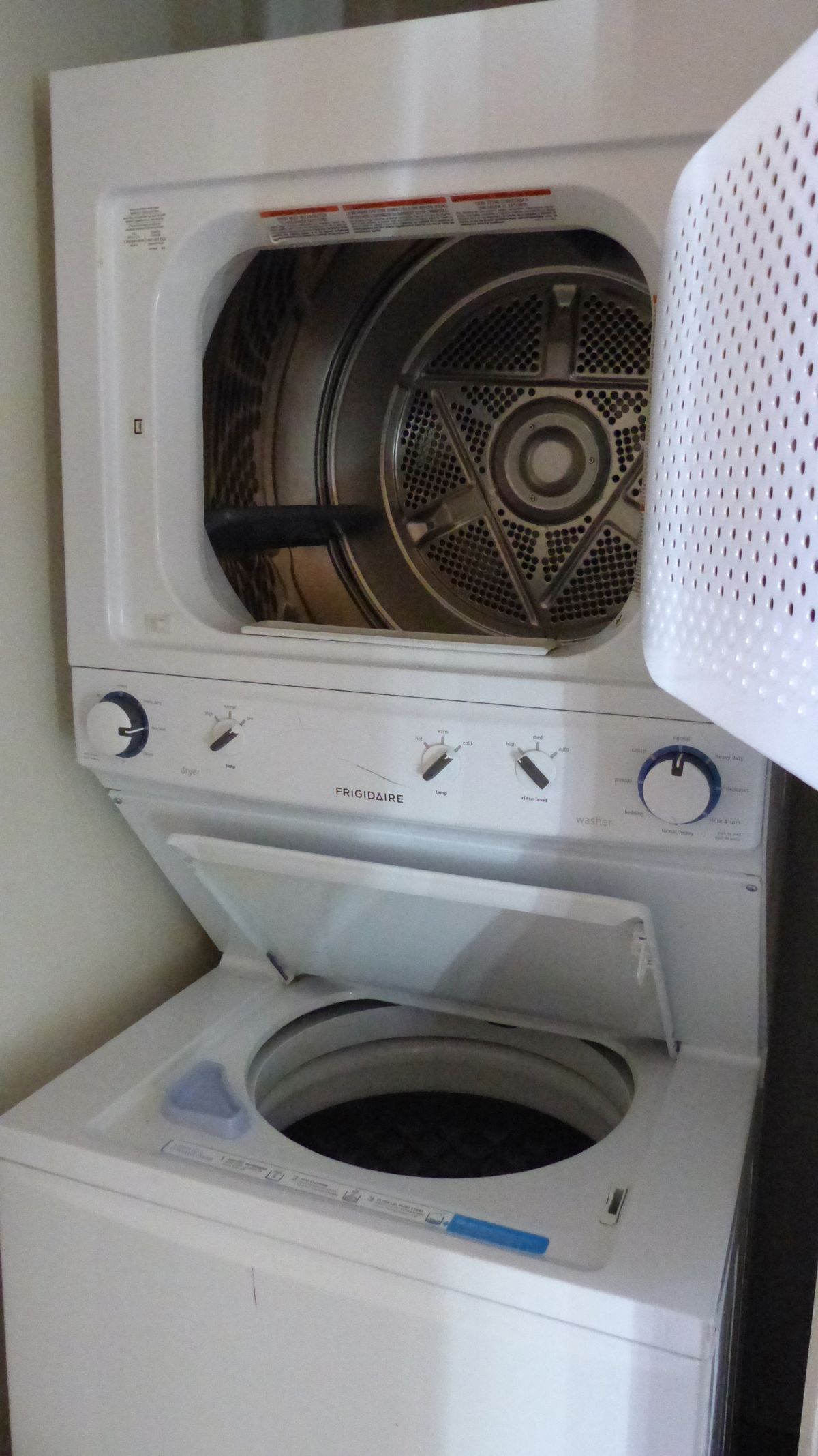 A white stacked washer-dryer unit with the dryer door open, revealing the empty metal drum inside.
