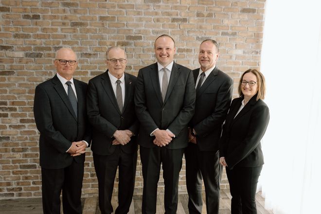 Five professionals in dark suits posing together against a brick wall