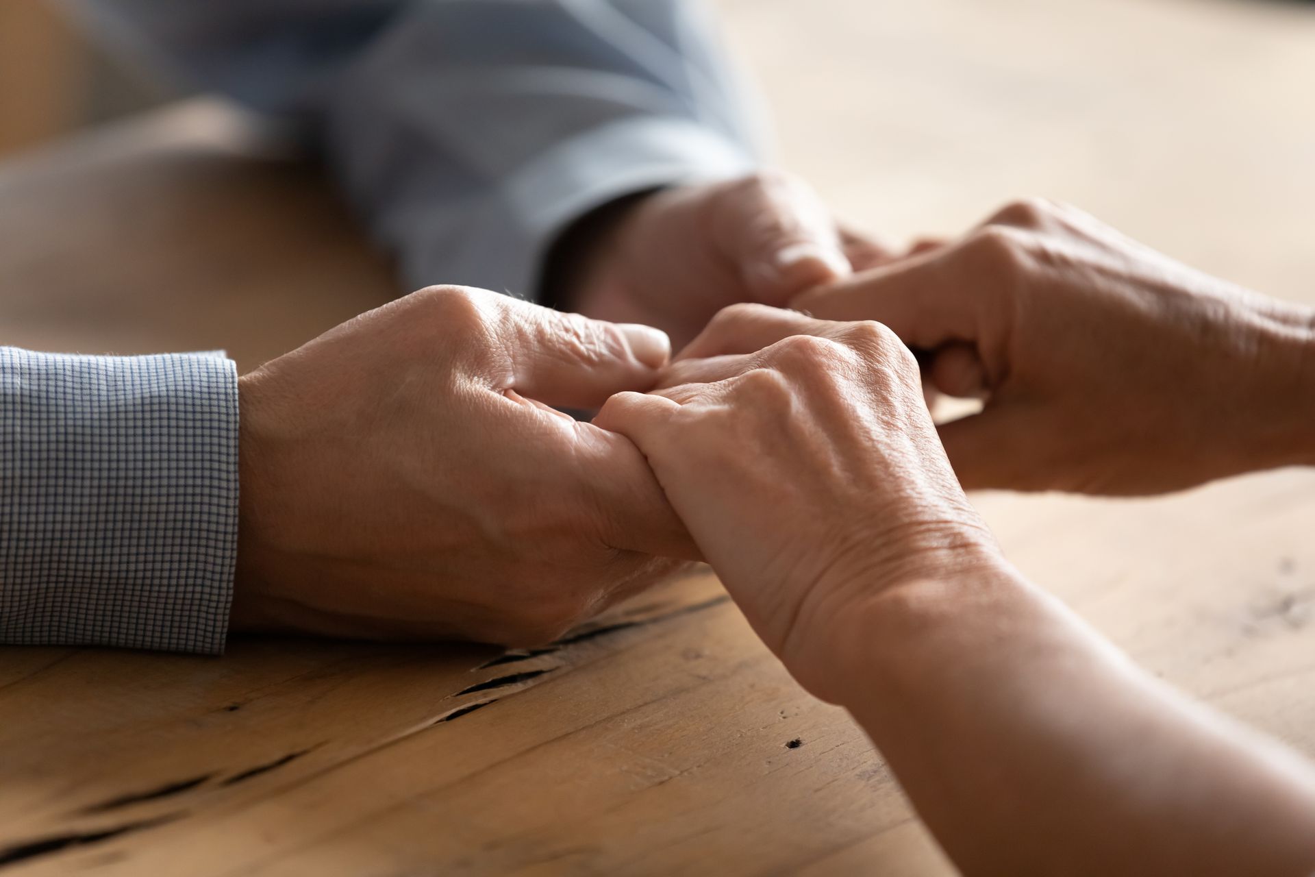 Hands clasped together on a wooden table in a close-up shot