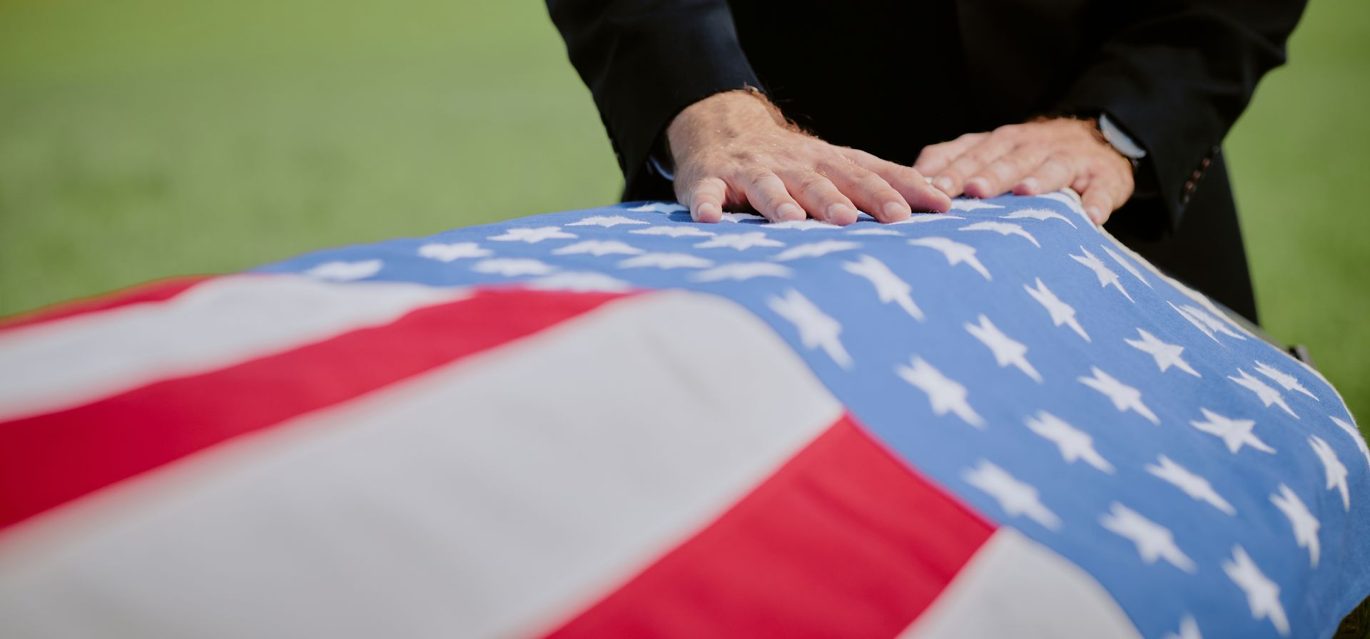 Hands resting on a U.S. flag-draped casket during a funeral
