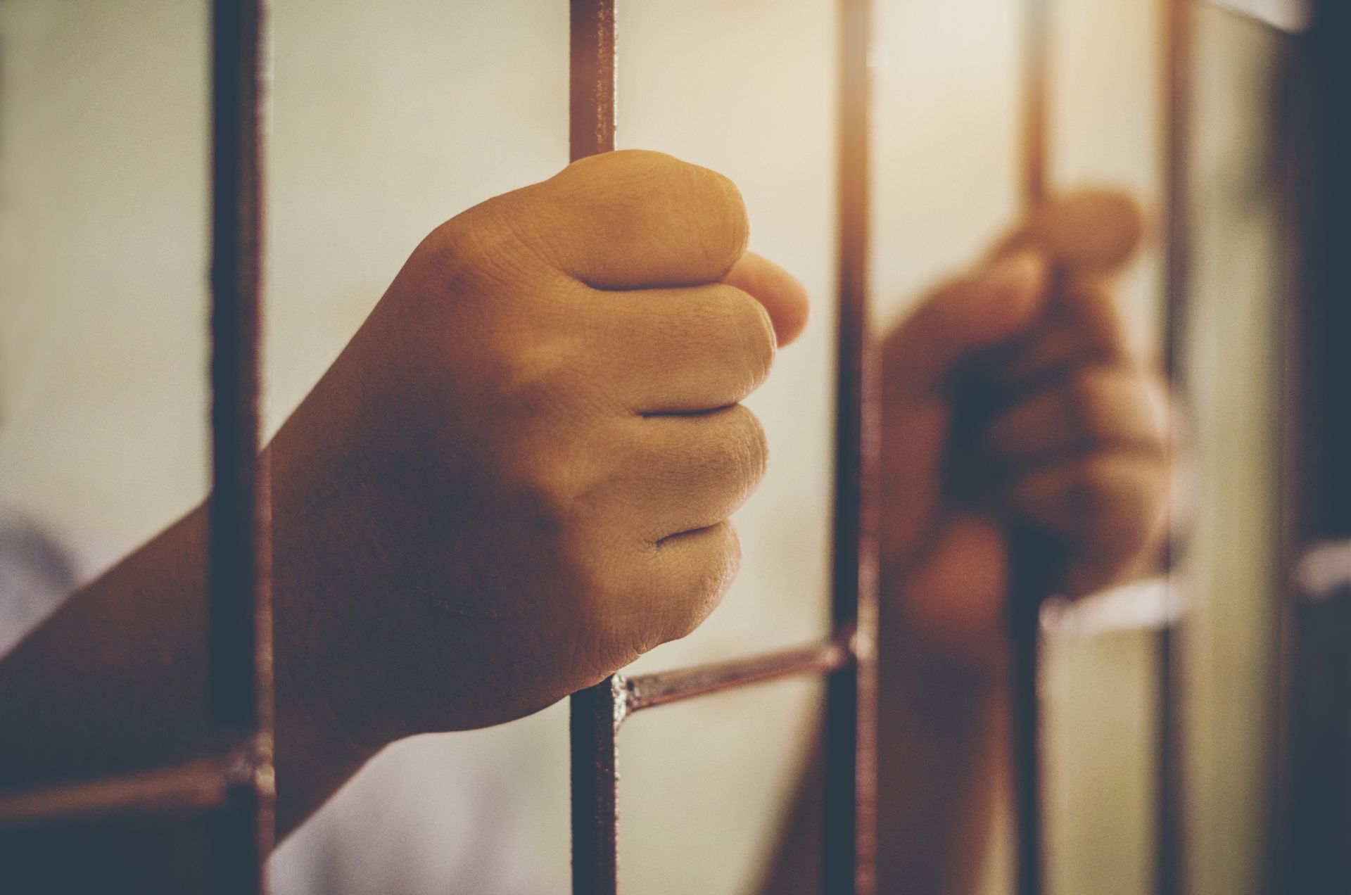 A person is holding onto the bars of a prison cell.