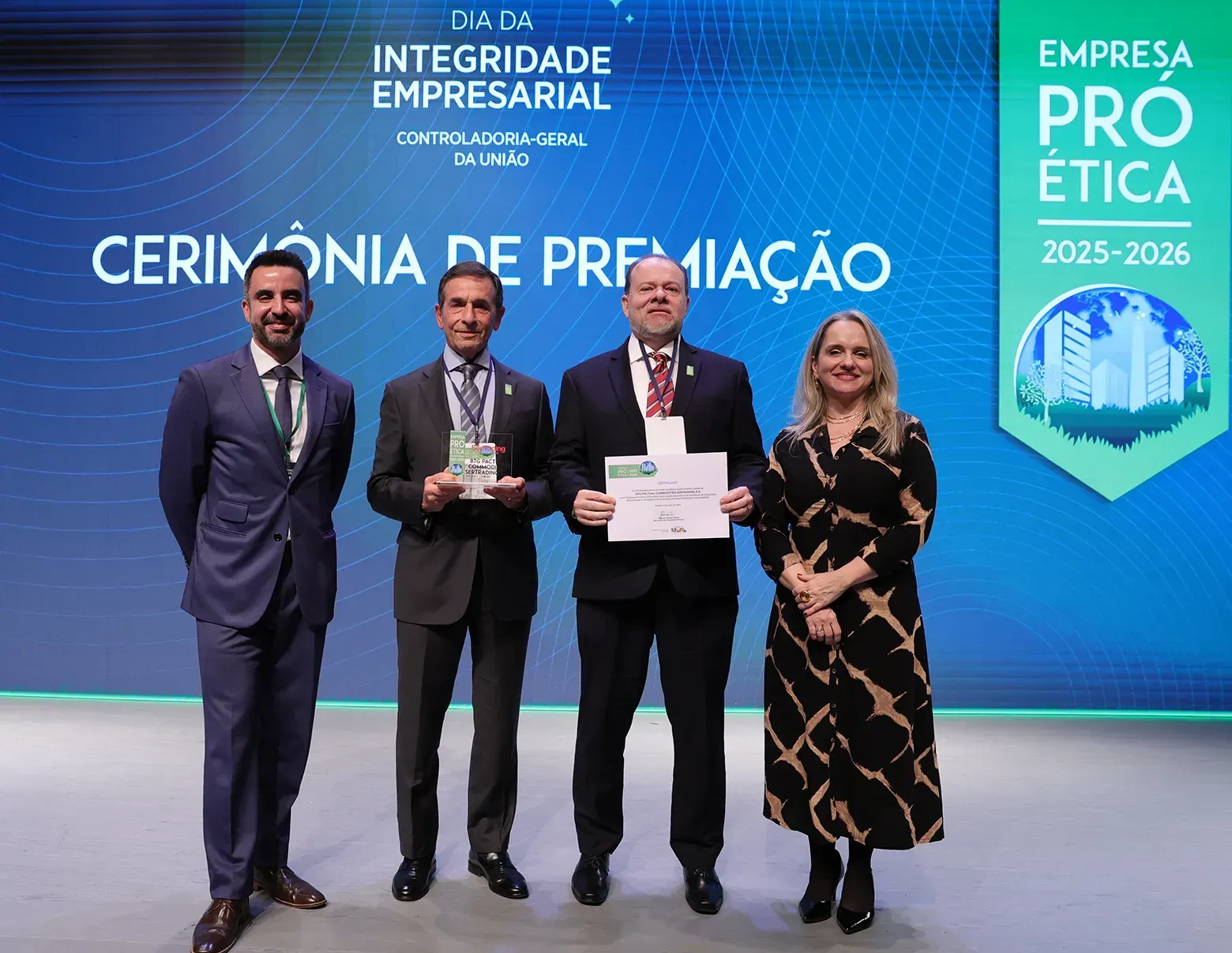 Quatro pessoas posam em cerimônia de premiação com troféu e certificado, diante de painel azul de sustentabilidade.