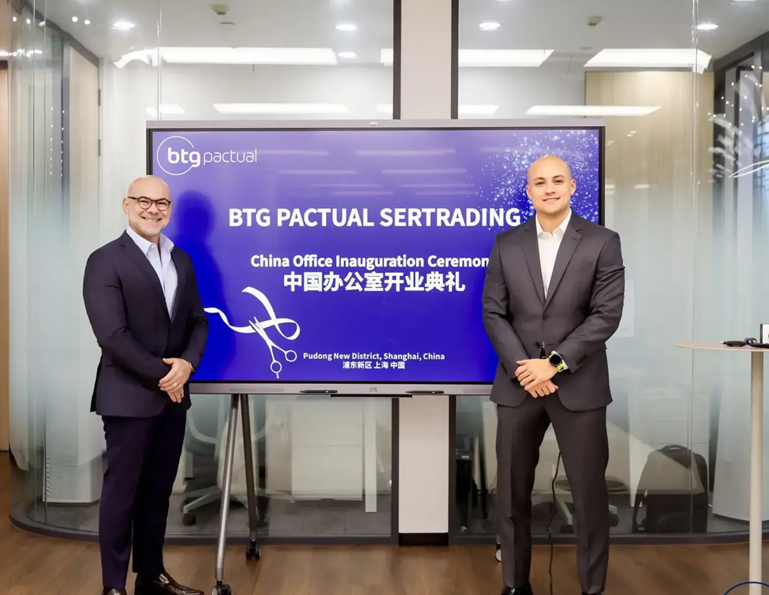 Homens de terno ao lado de tela com a inscrição “BTG Pactual Sertrading