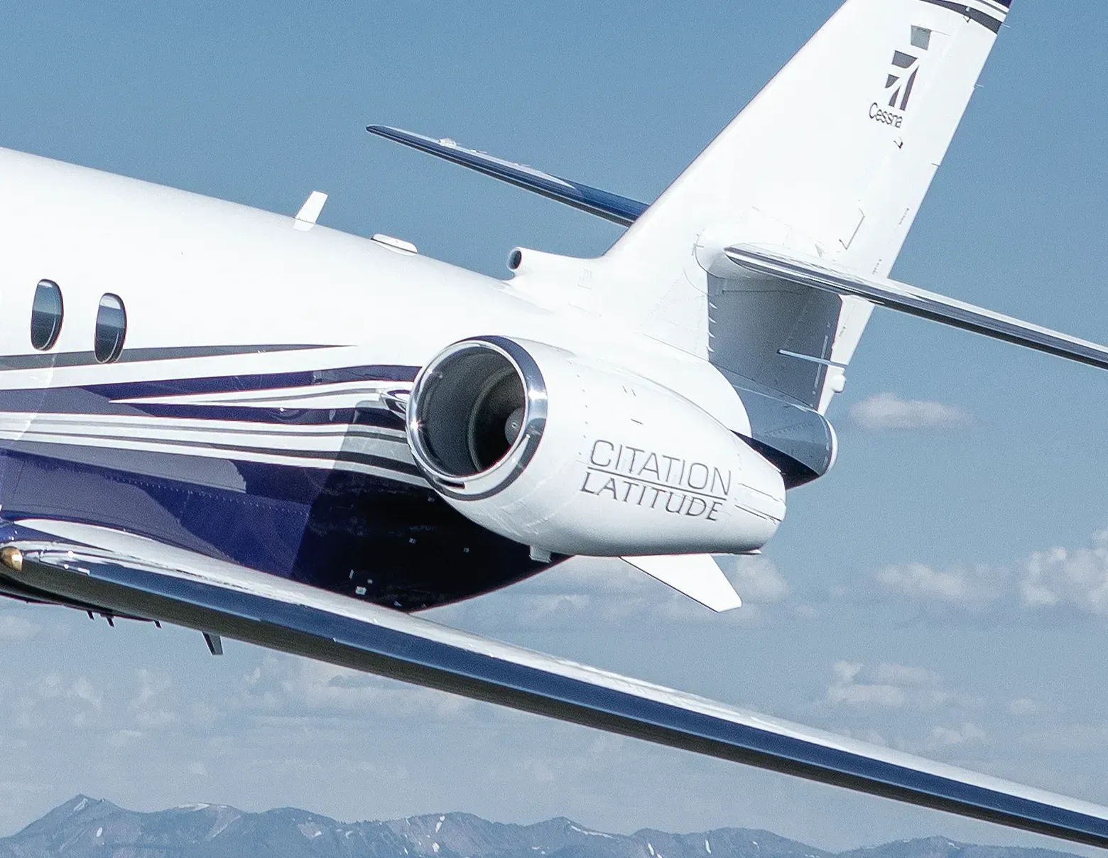 Close-up of a white private jet with blue stripes flying over mountains and blue sky
Close-up de um jato particular branco com listras azuis voando sobre montanhas e céu azul CESSNA CITATION LATITUDE