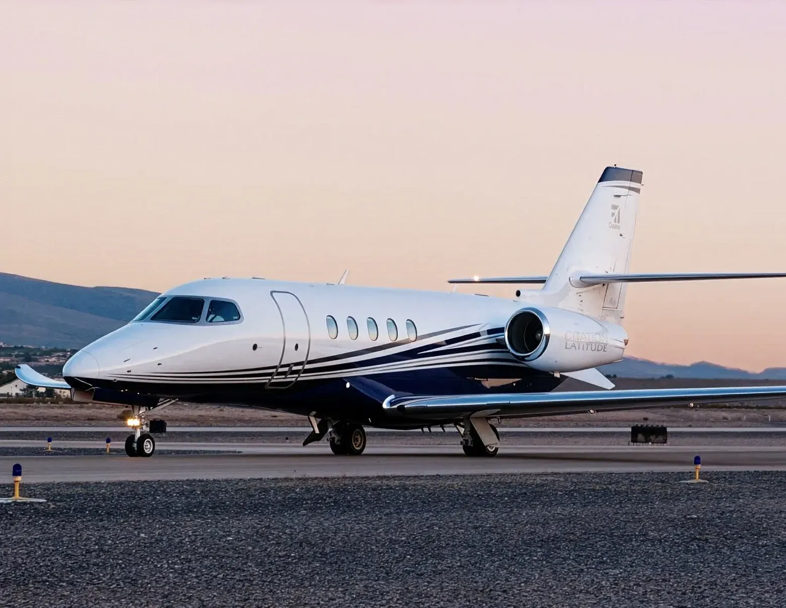 Jato executivo branco estacionado em uma pista ao pôr do sol, com montanhas ao fundo