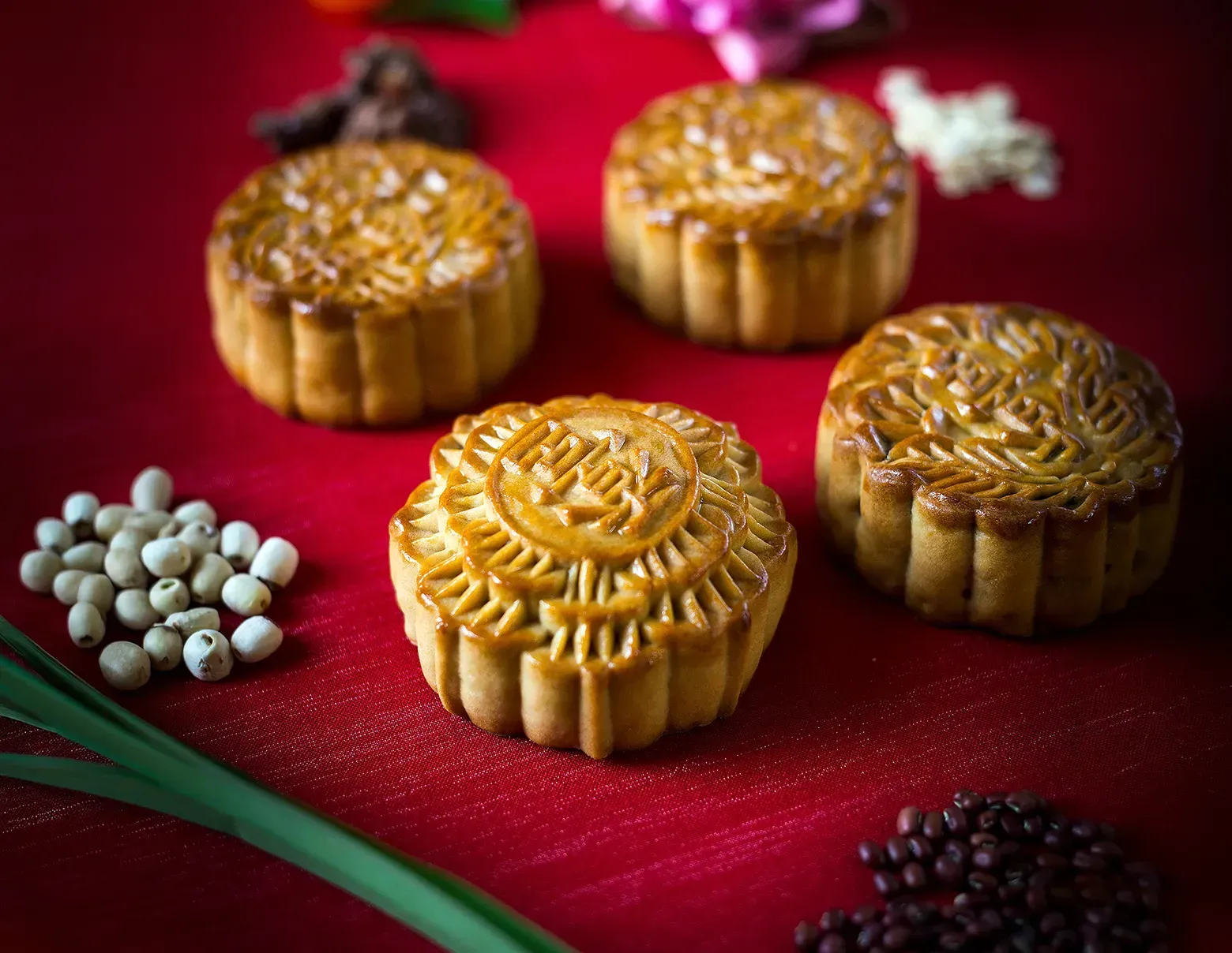 Golden mooncakes on a red cloth with white flowers and dark berries, arranged for a festive display