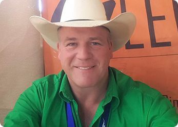 Man wearing a cowboy hat and green shirt smiling. Blue lanyard visible.