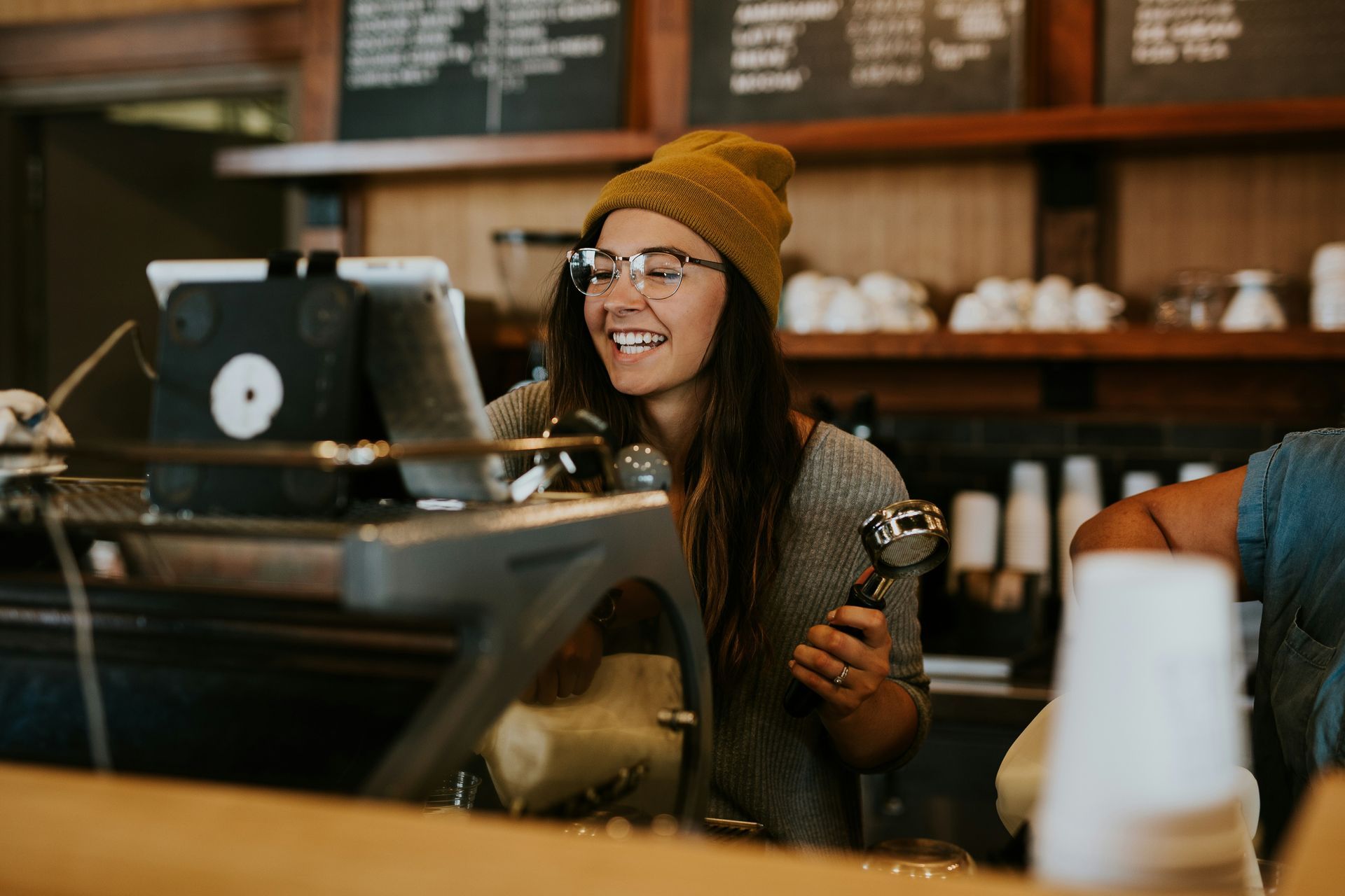 A woman is standing behind a counter in a coffee shop holding a cup of coffee.