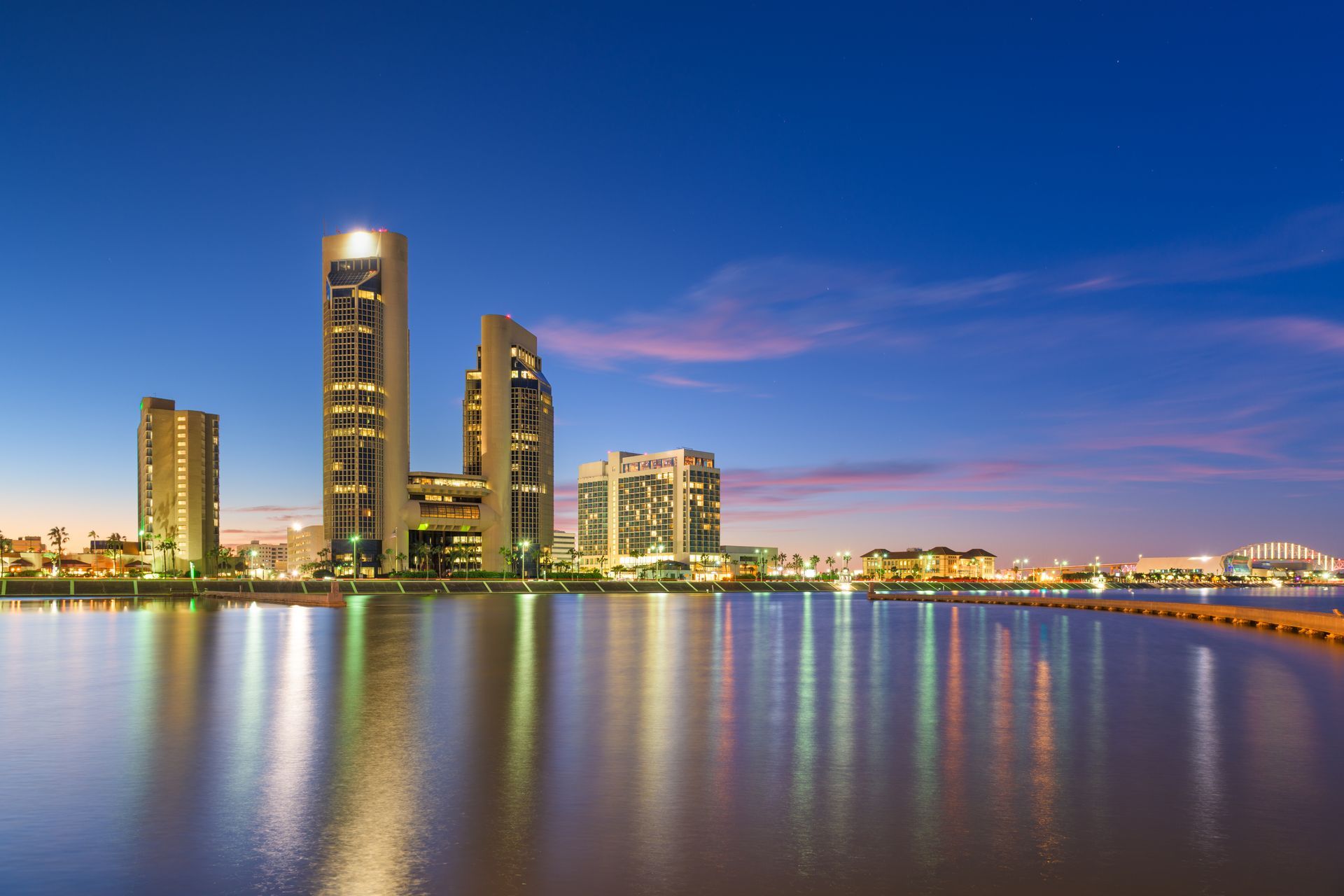 A city skyline at night with a body of water in the foreground.