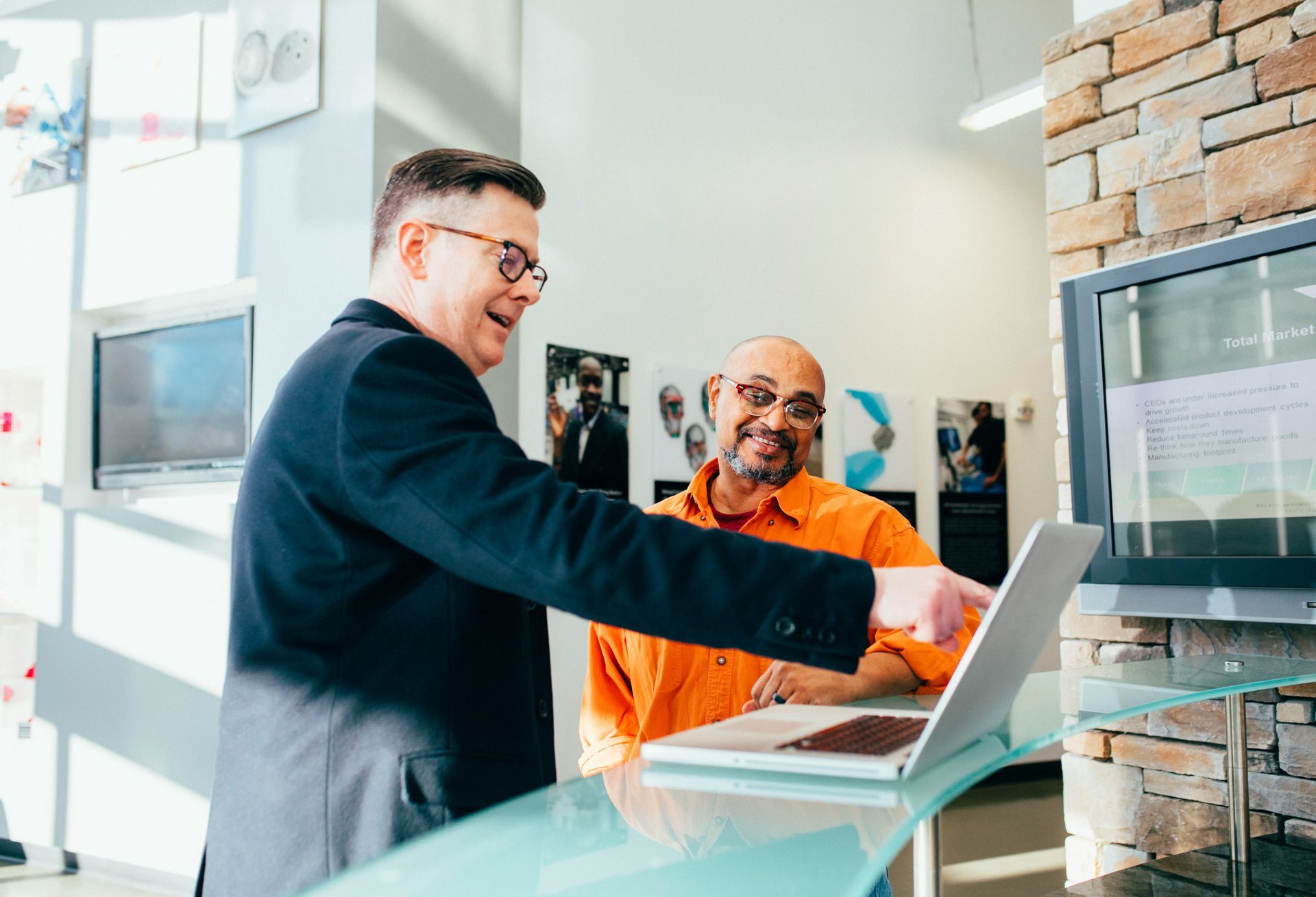 A man is pointing at a laptop computer while another man looks on.