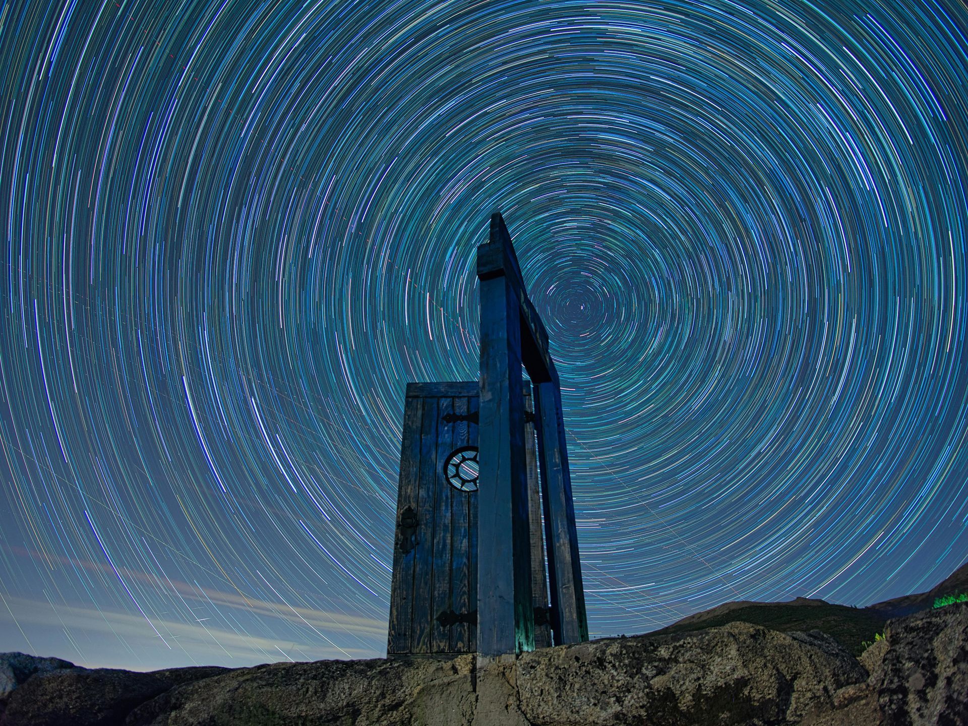Tall dark tower under a starry night sky with circular star trails over mountains