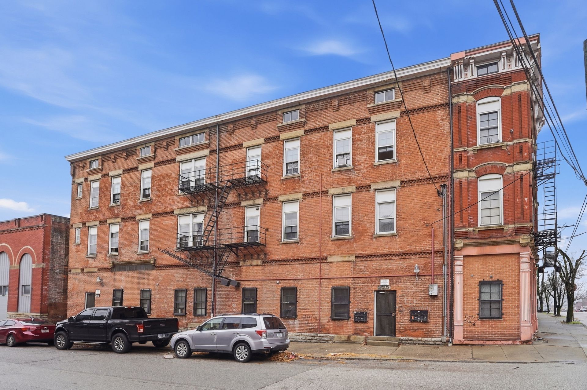 Red brick multi-story building with multiple rectangular windows against a blue cloudy sky.