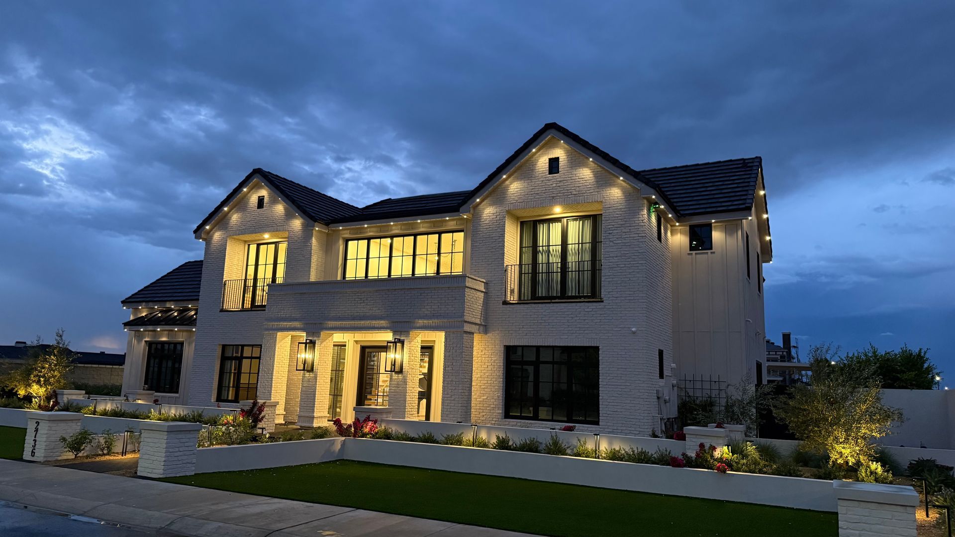 Illuminated modern farmhouse at dusk with bright windows and a manicured front lawn