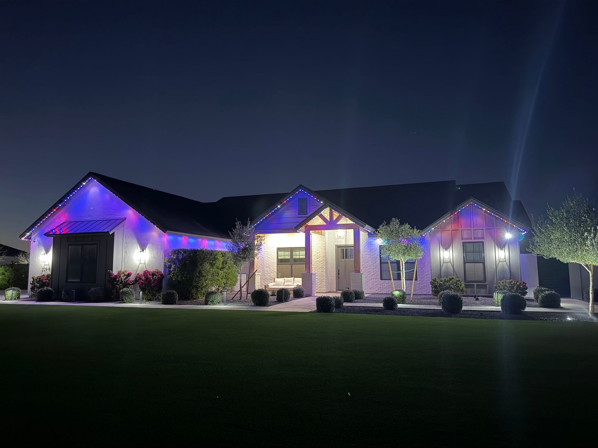 Single-story house at night with purple holiday lights and a lit front entrance