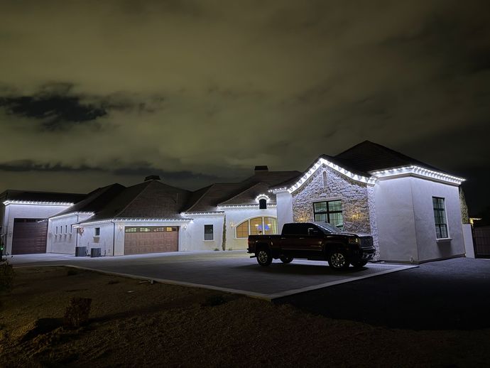 Suburban house at night with white holiday lights and a black SUV in the driveway