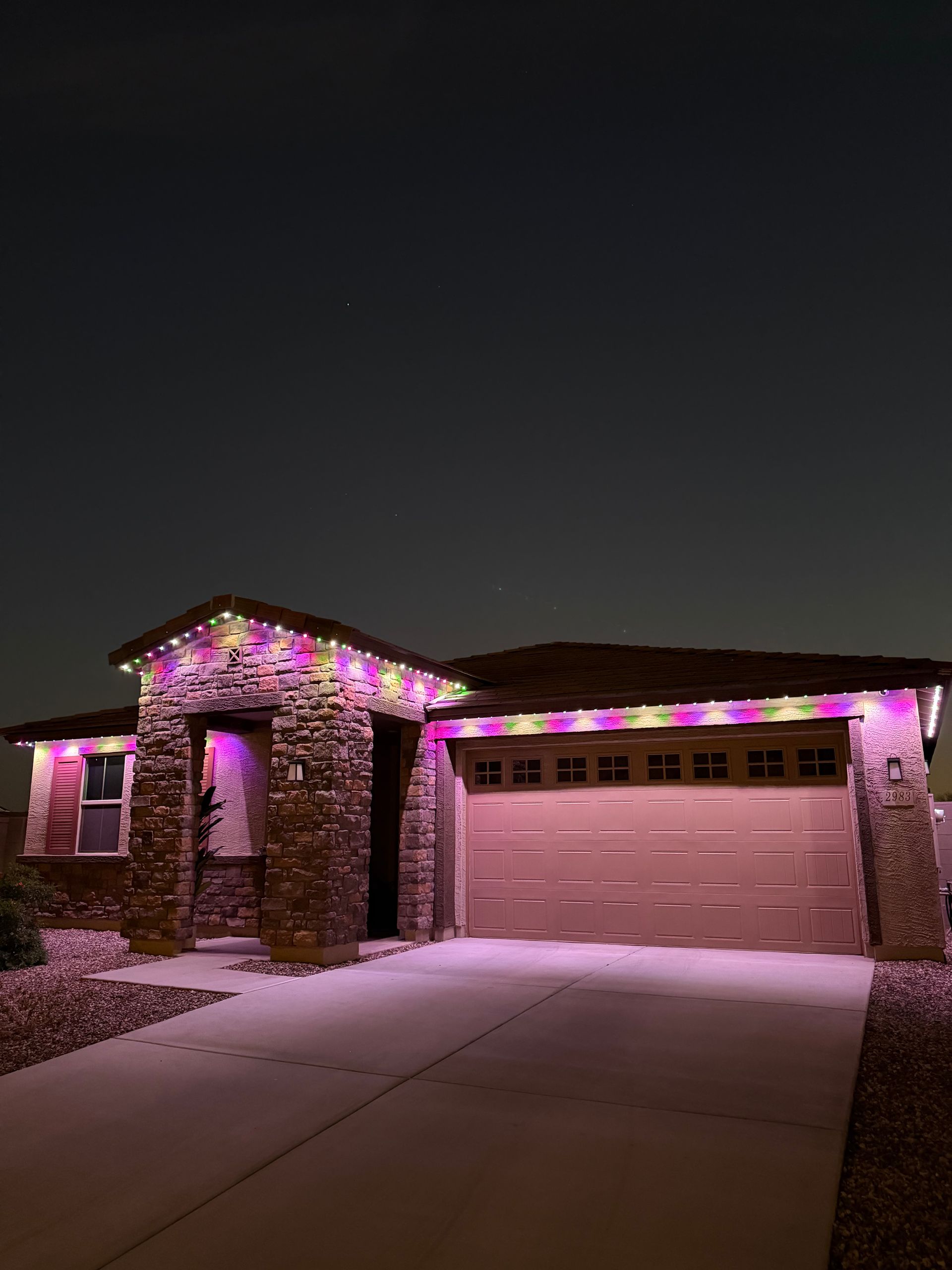 House and garage decorated with purple Christmas lights at night, with a snow-dusted driveway