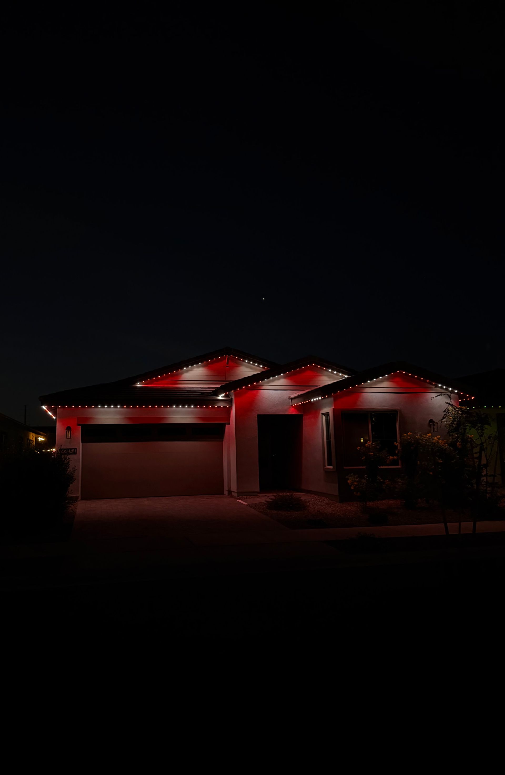 House at night with red roof lights and a dark front yard