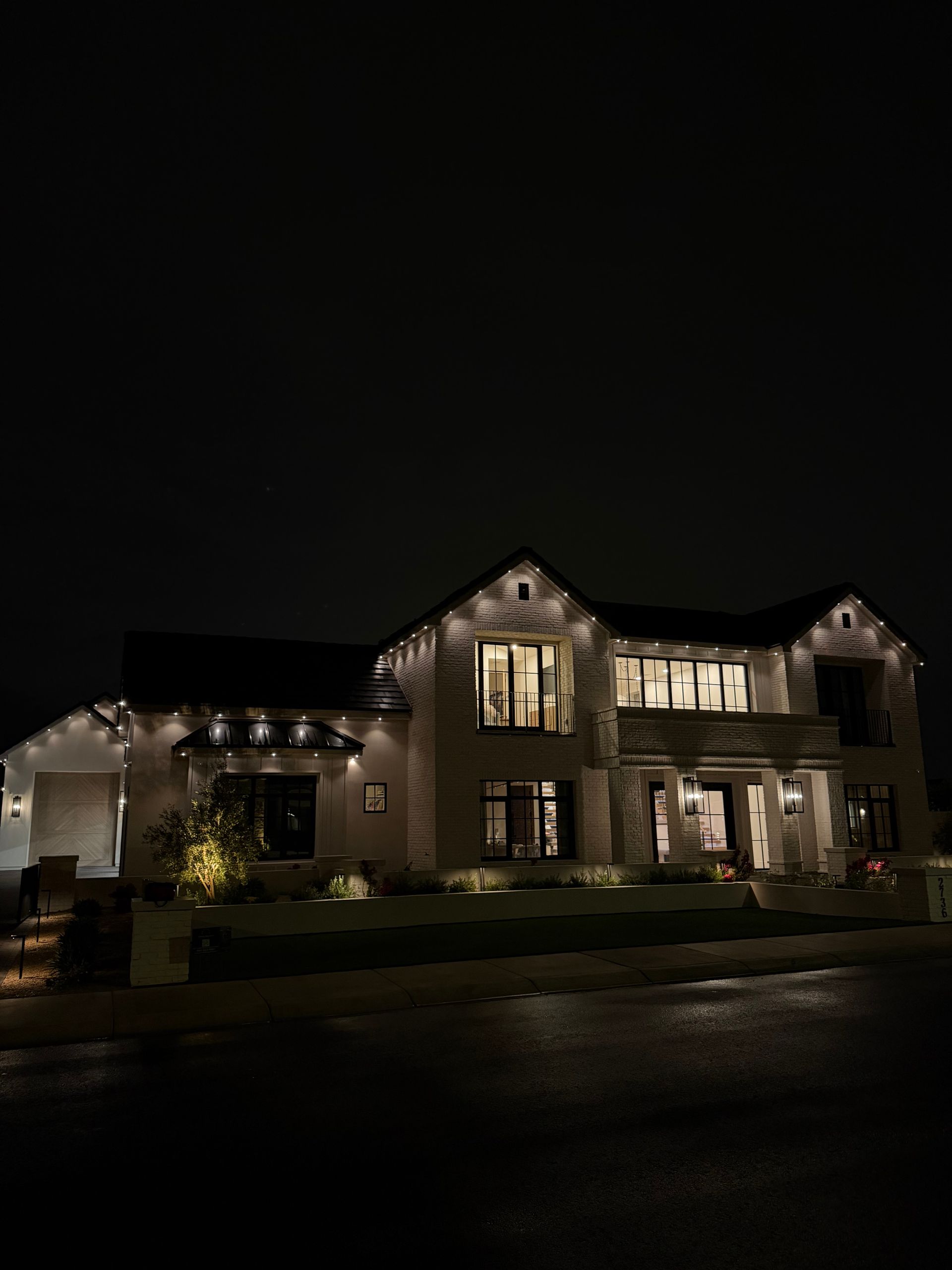 Large two-story house lit with warm exterior lights at night, viewed from the street