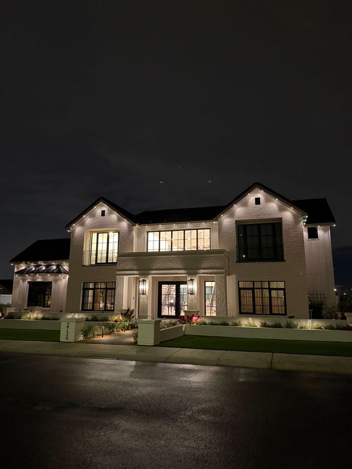Large lit suburban house at night with a brick facade and wet driveway