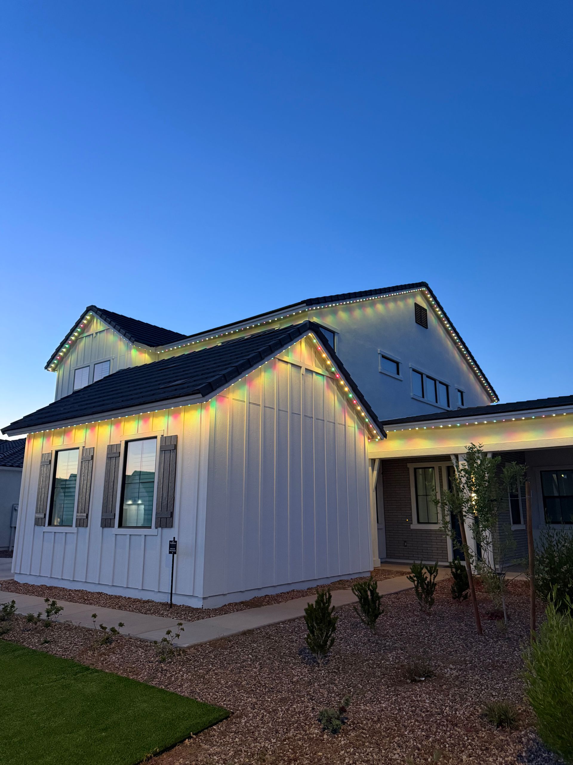 White house exterior at dusk with warm roofline lights, blue sky, and gravel landscaping.