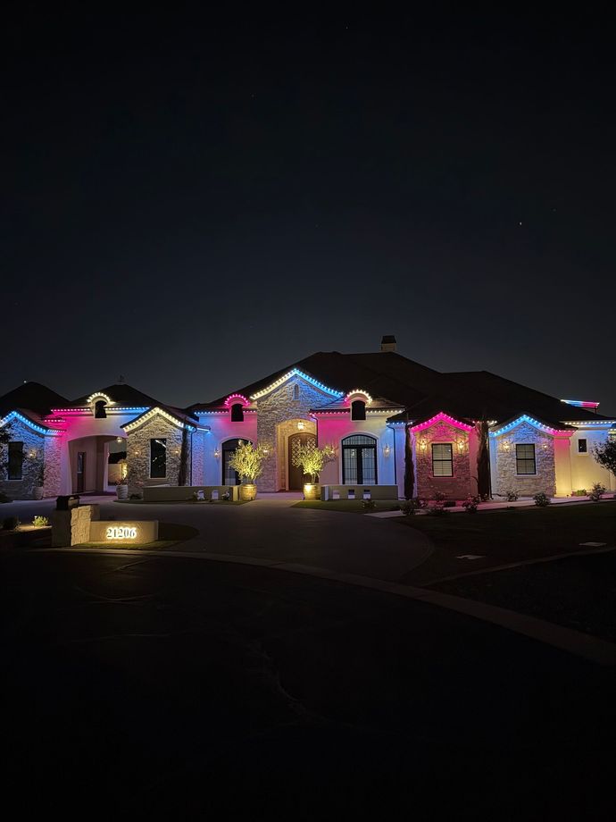 Holiday-lit row of houses at night, glowing with multicolored Christmas lights under a dark sky