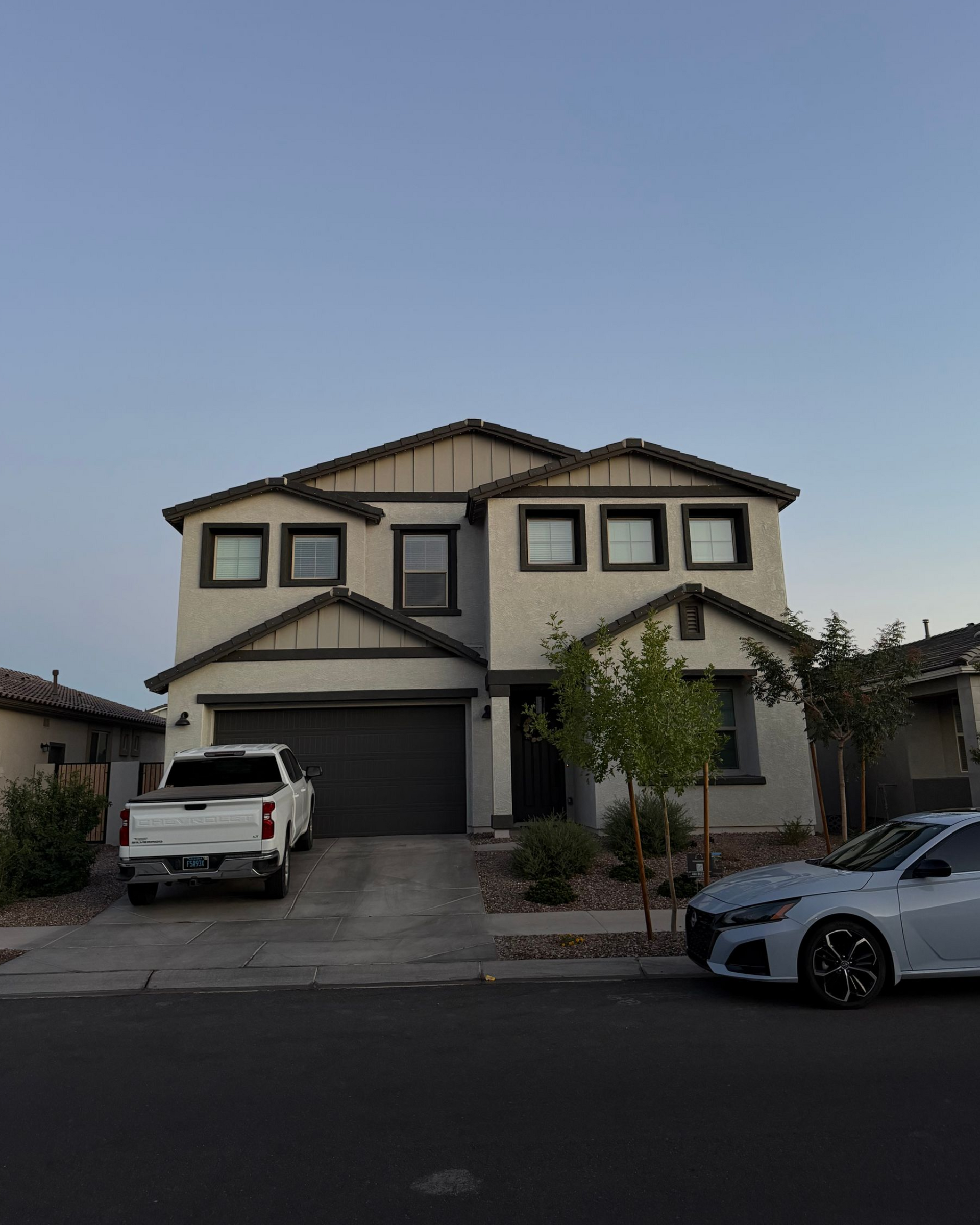 Two-story suburban house with two cars parked in the driveway at dusk