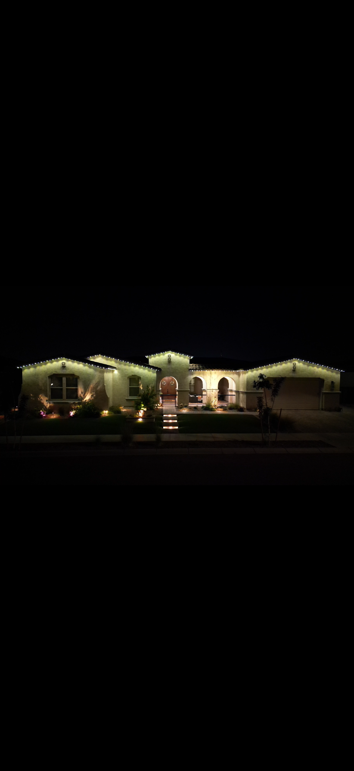 Single-story house at night, lit by warm exterior lights against a dark sky.